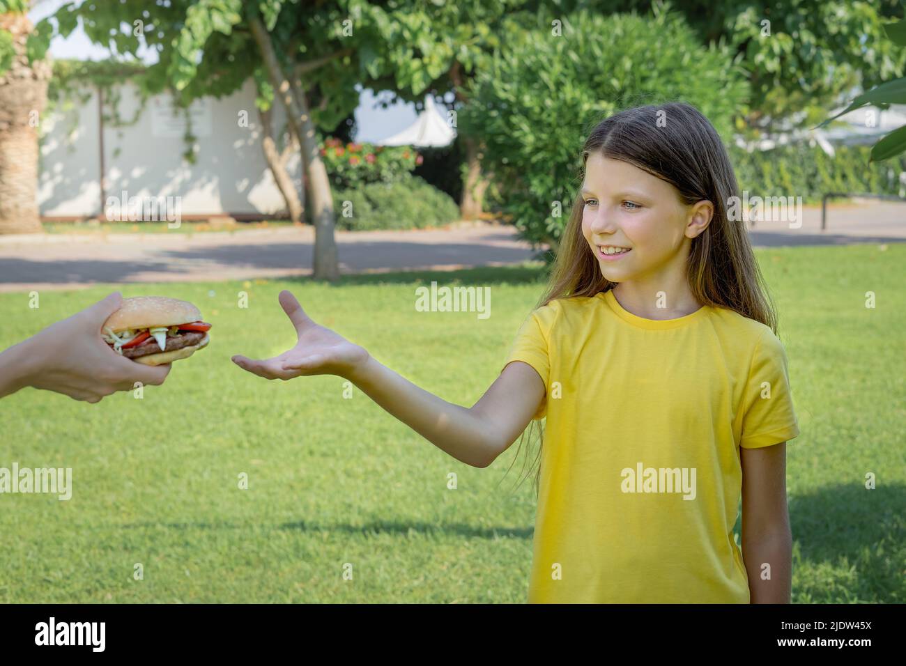 Una ragazza adolescente raggiunge per un hamburger con la mano. Messa a fuoco selettiva. Foto Stock