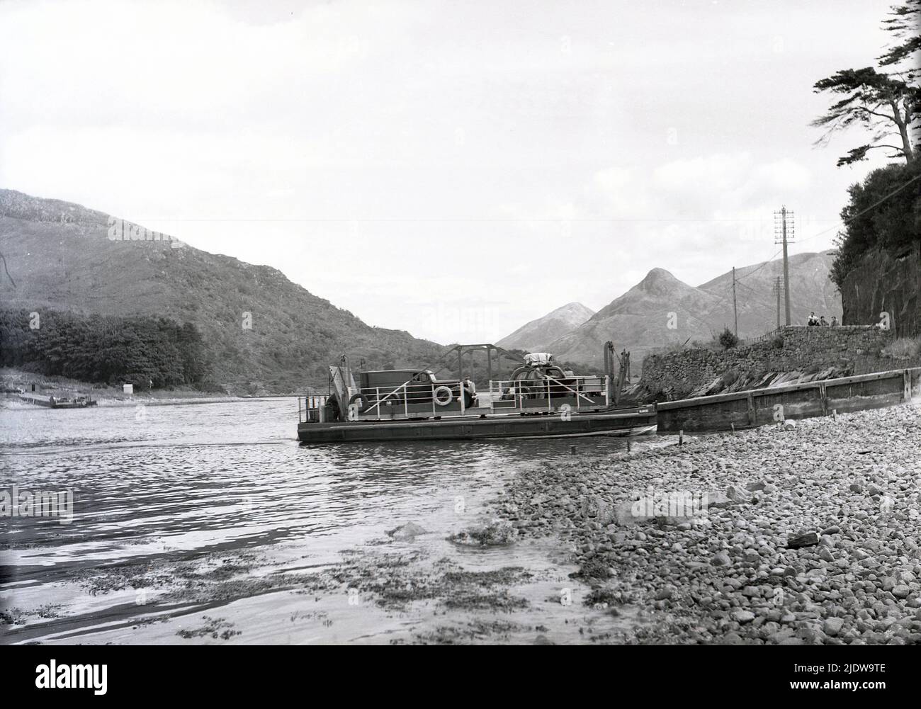 1950s, storico, un piccolo attracco di traghetto per auto a piattaforma in riva al fiume, Scottish Highlands, Scozia, Regno Unito. Delle centinaia di isole scozzesi al largo, 95 sono abitate tutto l'anno e molte di queste comunità remote possono essere raggiunte solo con questi piccoli traghetti. Foto Stock