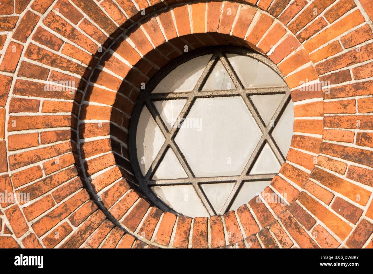 Vista di un segno pentagramma e simbolo su una vecchia finestra rotonda su un muro di mattoni rossi. Vetro d'epoca con telaio in metallo e pentagono sulla chiesa storica Foto Stock