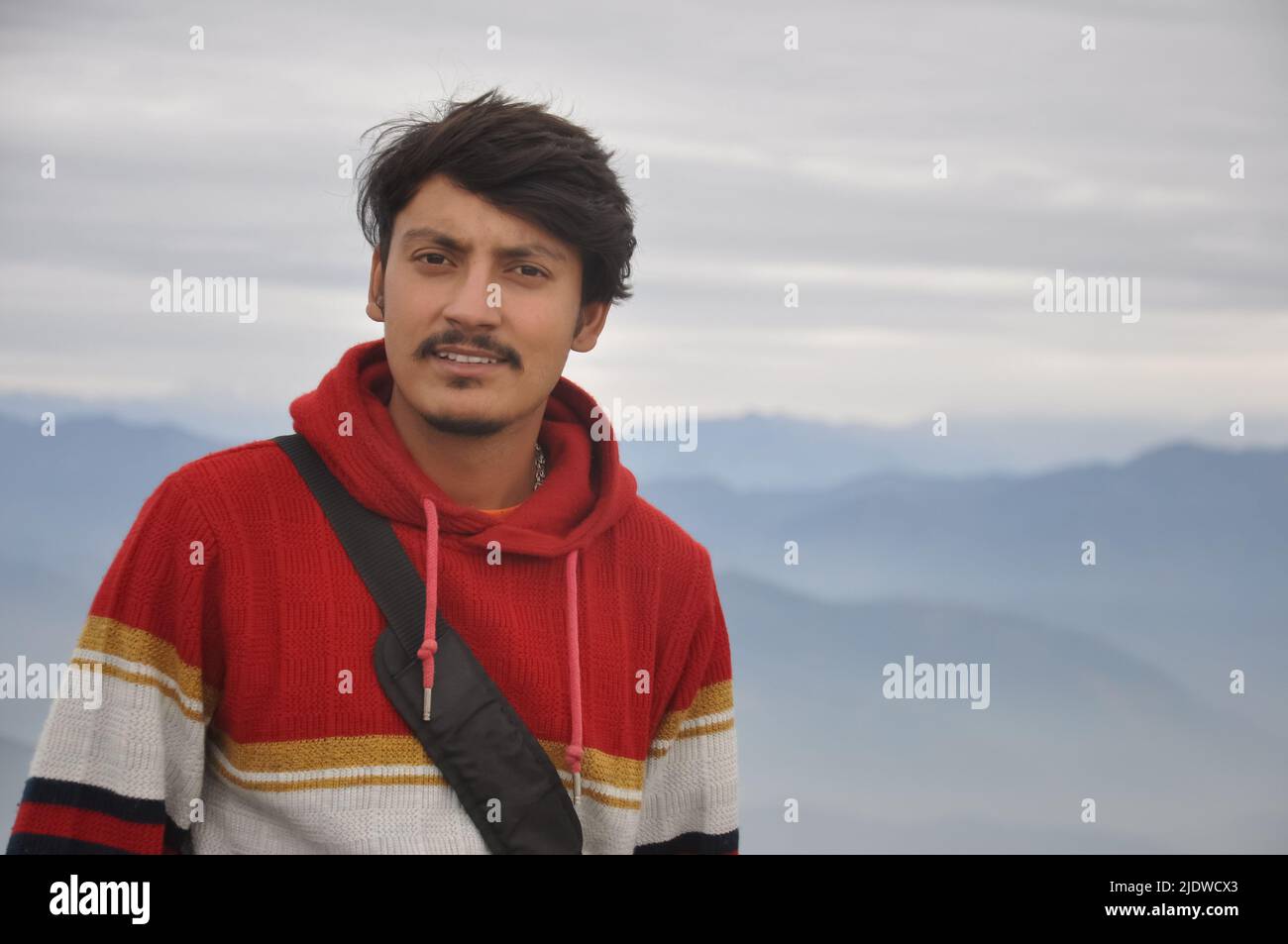 Primo piano di un bel giovane indiano che guarda la macchina fotografica mentre si alza sullo sfondo delle montagne Foto Stock