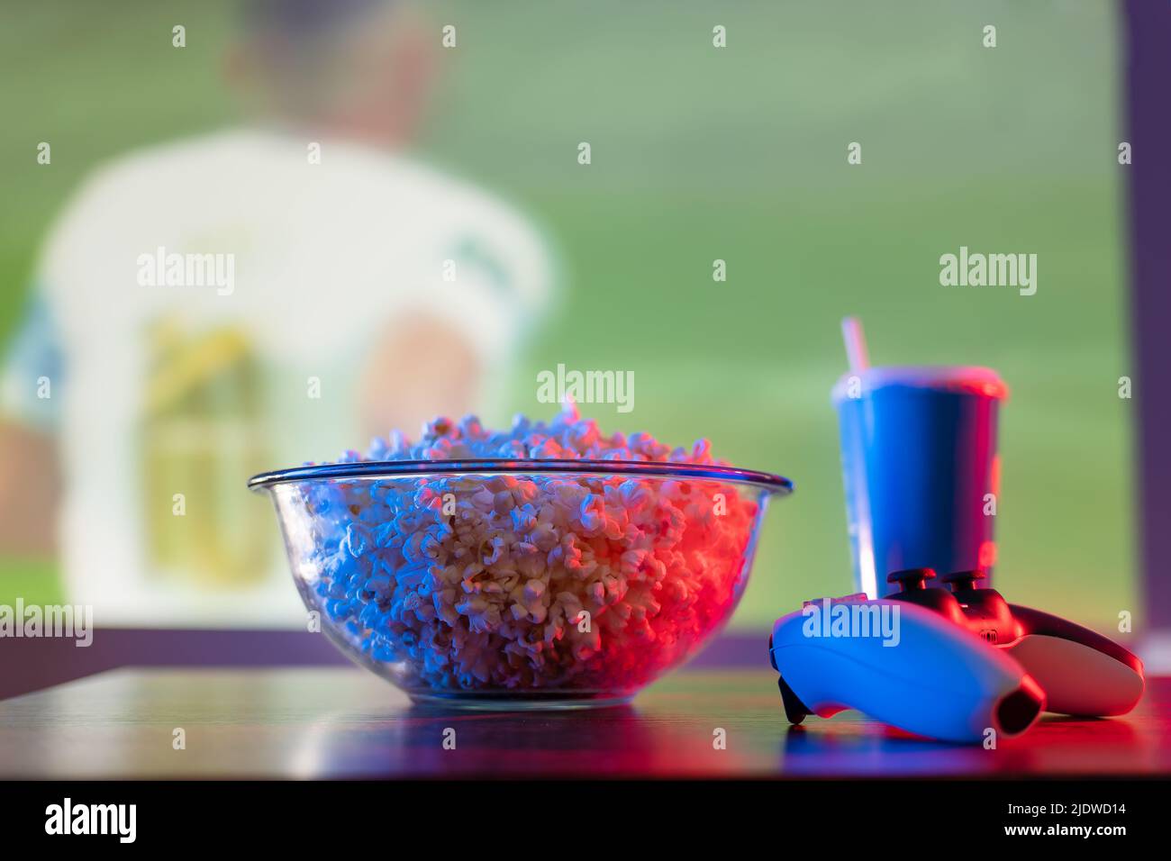 Sullo sfondo di una partita di calcio sul grande schermo TV: Popcorn, un drink e un joystick. Giochi sportivi, giochi online con gli amici, giochi sportivi Foto Stock