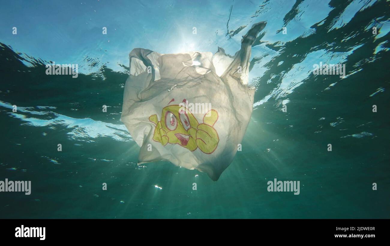 Inquinamento di plastica, sacchetto di plastica usato con il viso sorridente lentamente che si sgocciola sott'acqua ai raggi del sole all'alba. Scatto ad angolazione ridotta, retroilluminazione (Contre-jour). Plastica Foto Stock