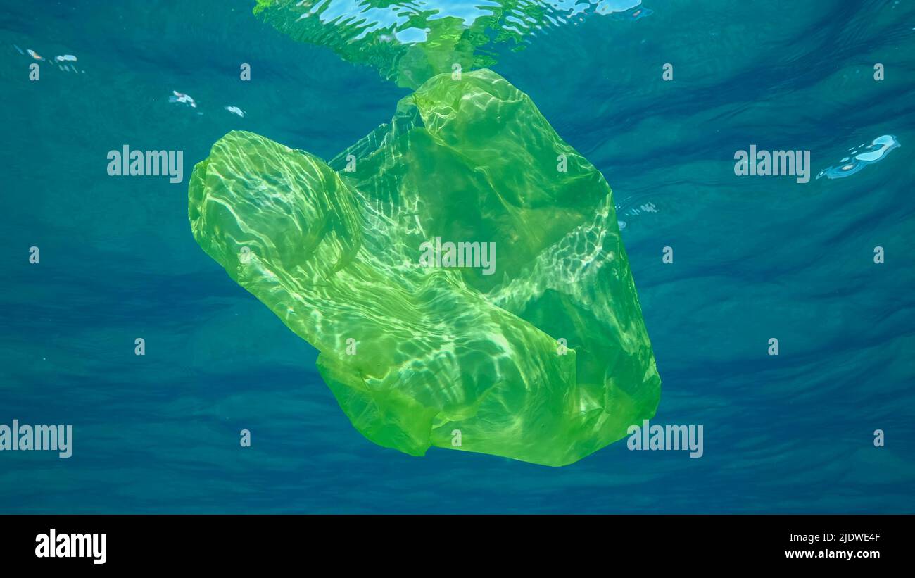 Inquinamento di plastica, sacchetto di plastica giallo nuota sott'acqua riflettendo sulla superficie dell'acqua blu nelle luci del sole. Gettare lentamente il sacchetto di plastica Foto Stock