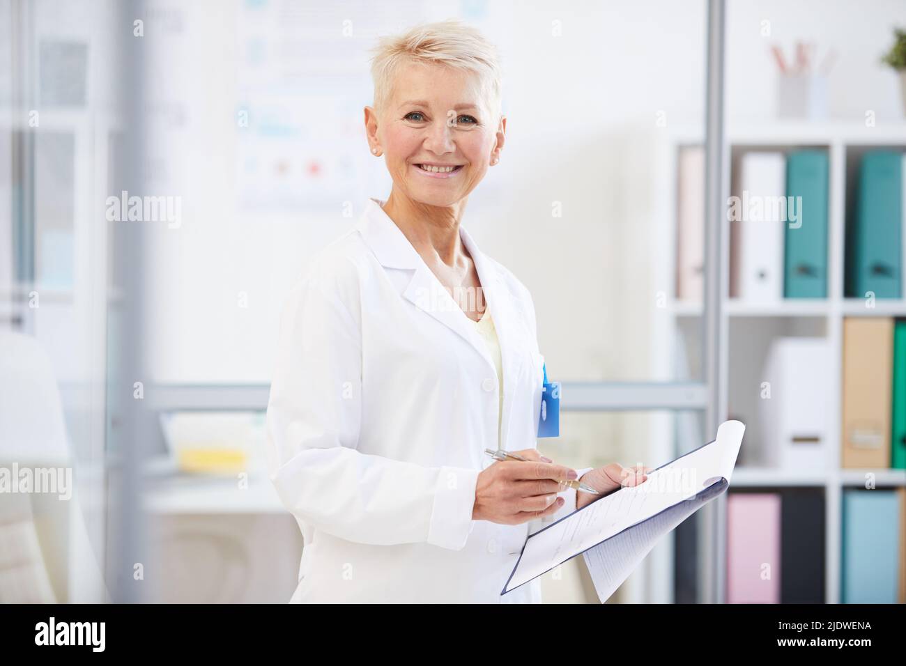 Ritratto di positivo sicuro medico femminile in camice da laboratorio in piedi in ufficio e di lavoro con file medici Foto Stock