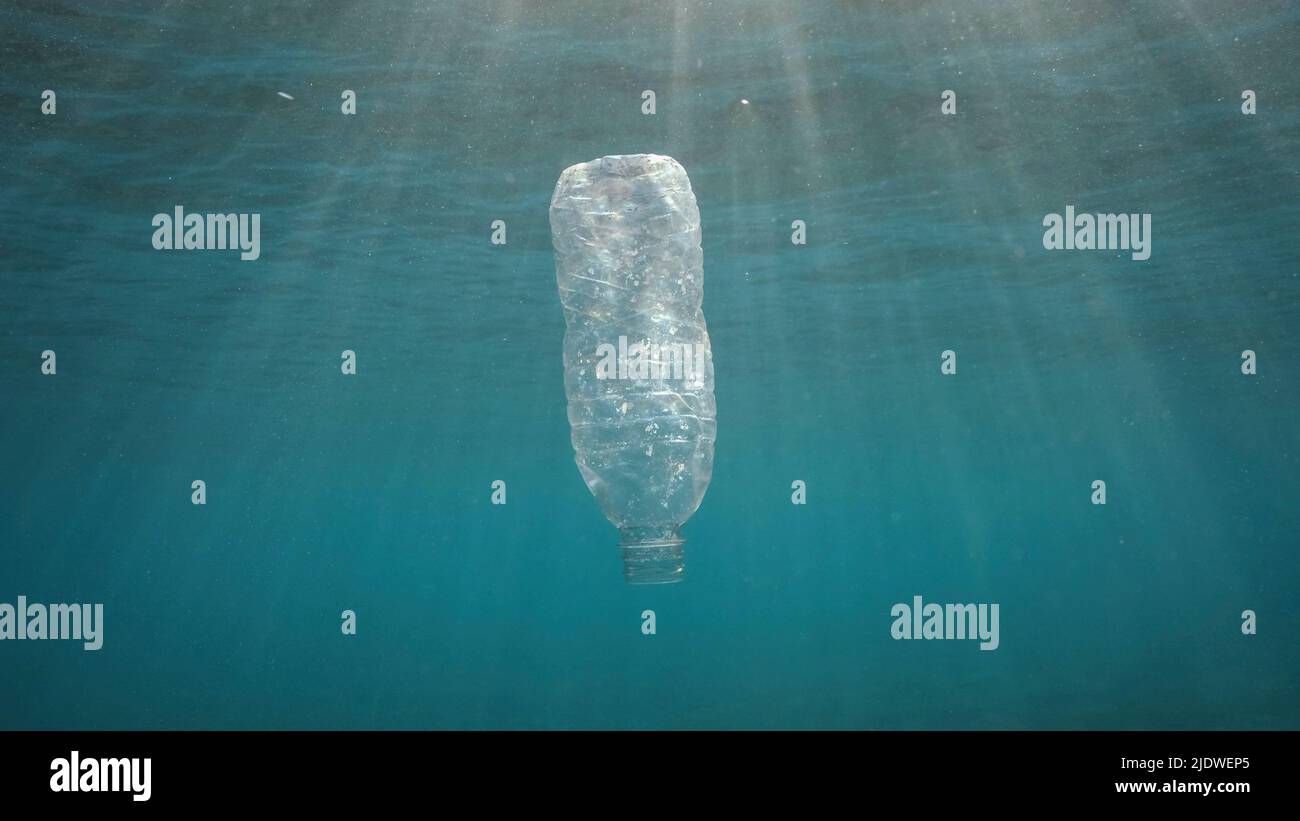 Inquinamento di plastica, bottiglia di plastica scartata che gocciola sotto la superficie dell'acqua a raggi solari al tramonto. Bottiglia di plastica in acqua blu. Rifiuti di plastica Foto Stock