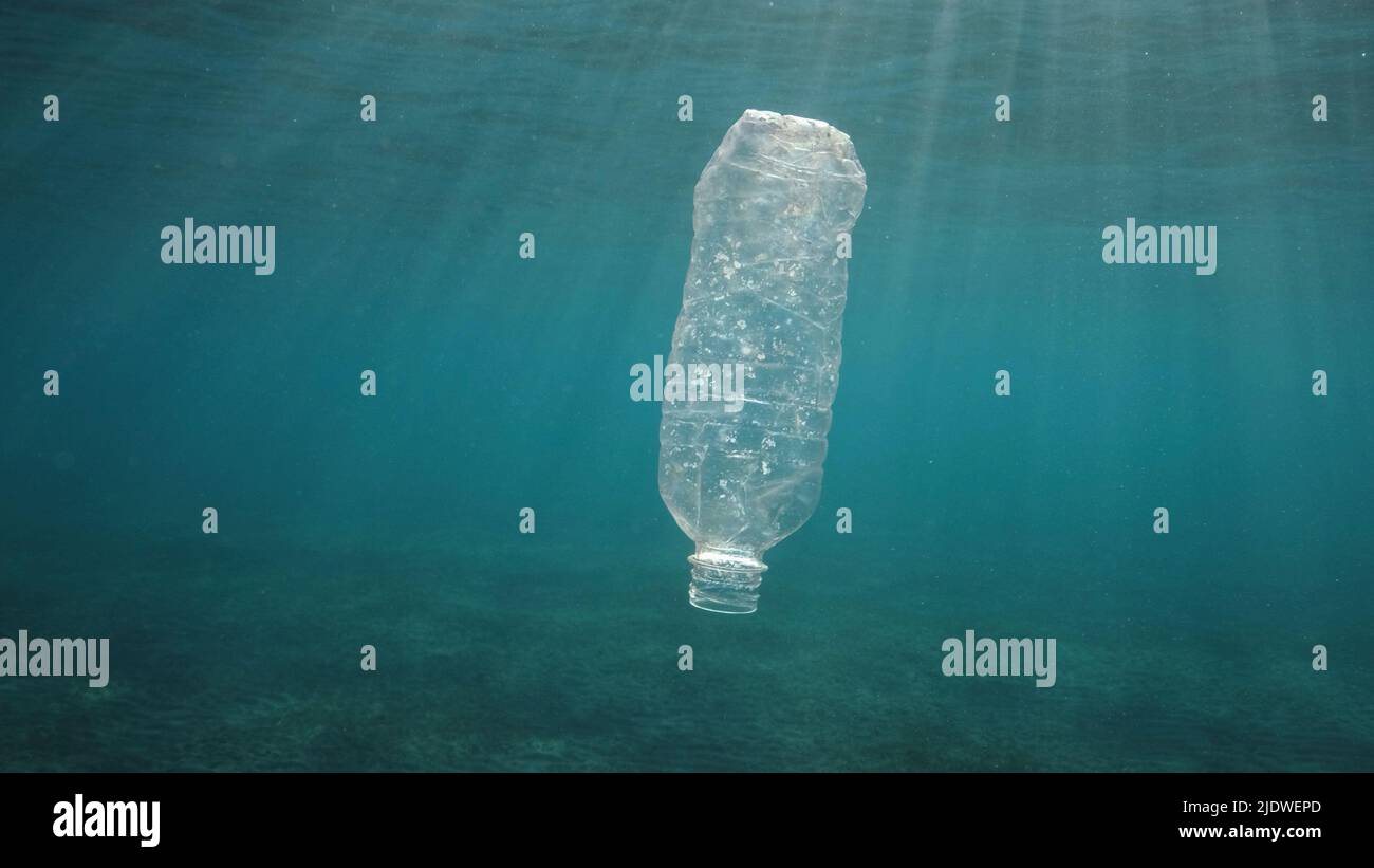 Inquinamento di plastica, bottiglia di plastica scartata che gocciola sotto la superficie dell'acqua a raggi solari al tramonto. Bottiglia di plastica in acqua blu. Rifiuti di plastica Foto Stock