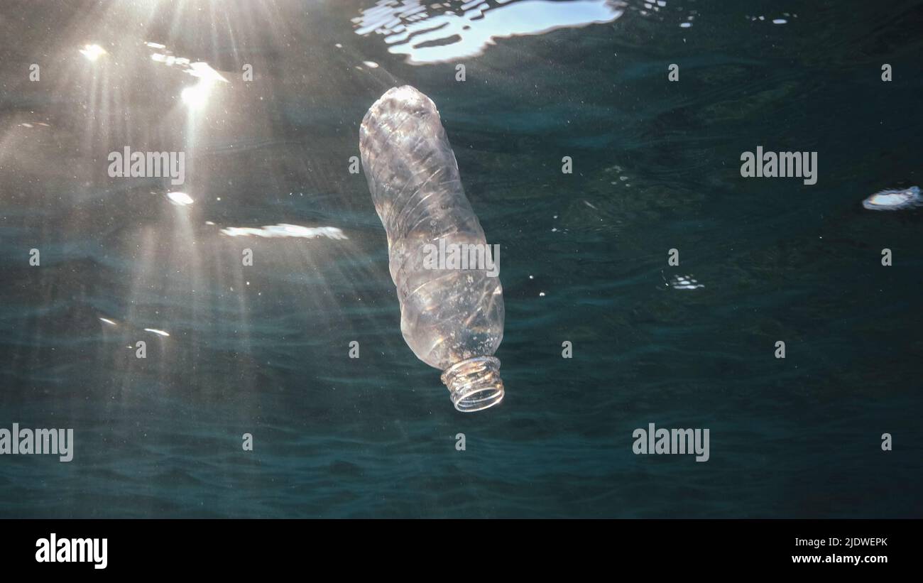 Inquinamento di plastica, bottiglia di plastica scartata che gocciola sotto la superficie dell'acqua a raggi solari al tramonto. Bottiglia di plastica in acqua blu. Rifiuti di plastica Foto Stock