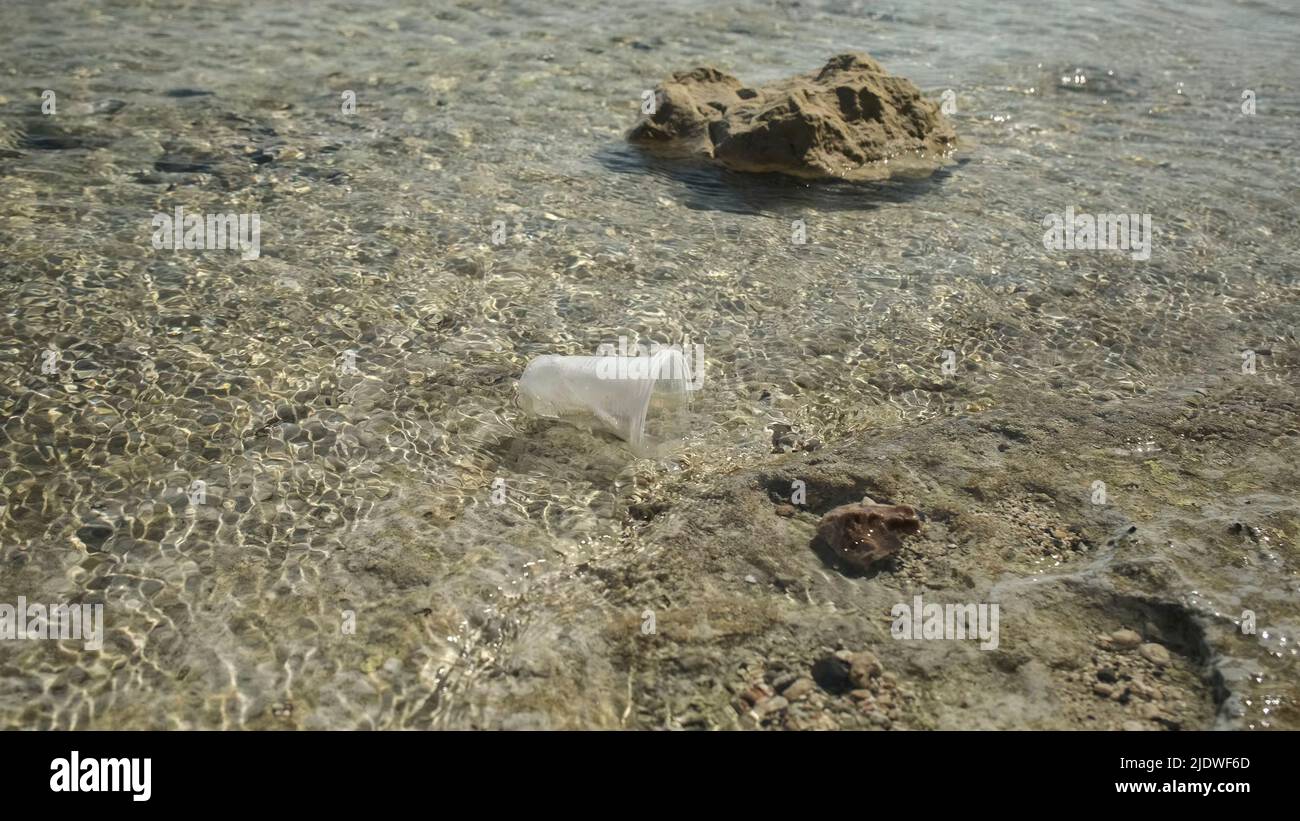 La coppa trasparente di plastica viene trasportata dal vento al mare nella zona costiera. Inquinamento plastico della zona surf. Mar Rosso, Egitto Foto Stock