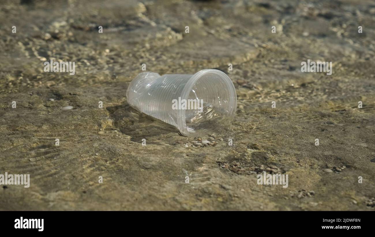 La coppa trasparente di plastica viene trasportata dal vento al mare nella zona costiera. Inquinamento plastico della zona surf. Mar Rosso, Egitto Foto Stock