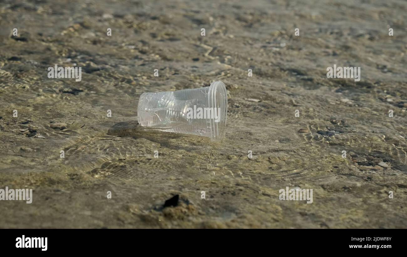 La coppa trasparente di plastica viene trasportata dal vento al mare nella zona costiera. Inquinamento plastico della zona surf. Mar Rosso, Egitto Foto Stock