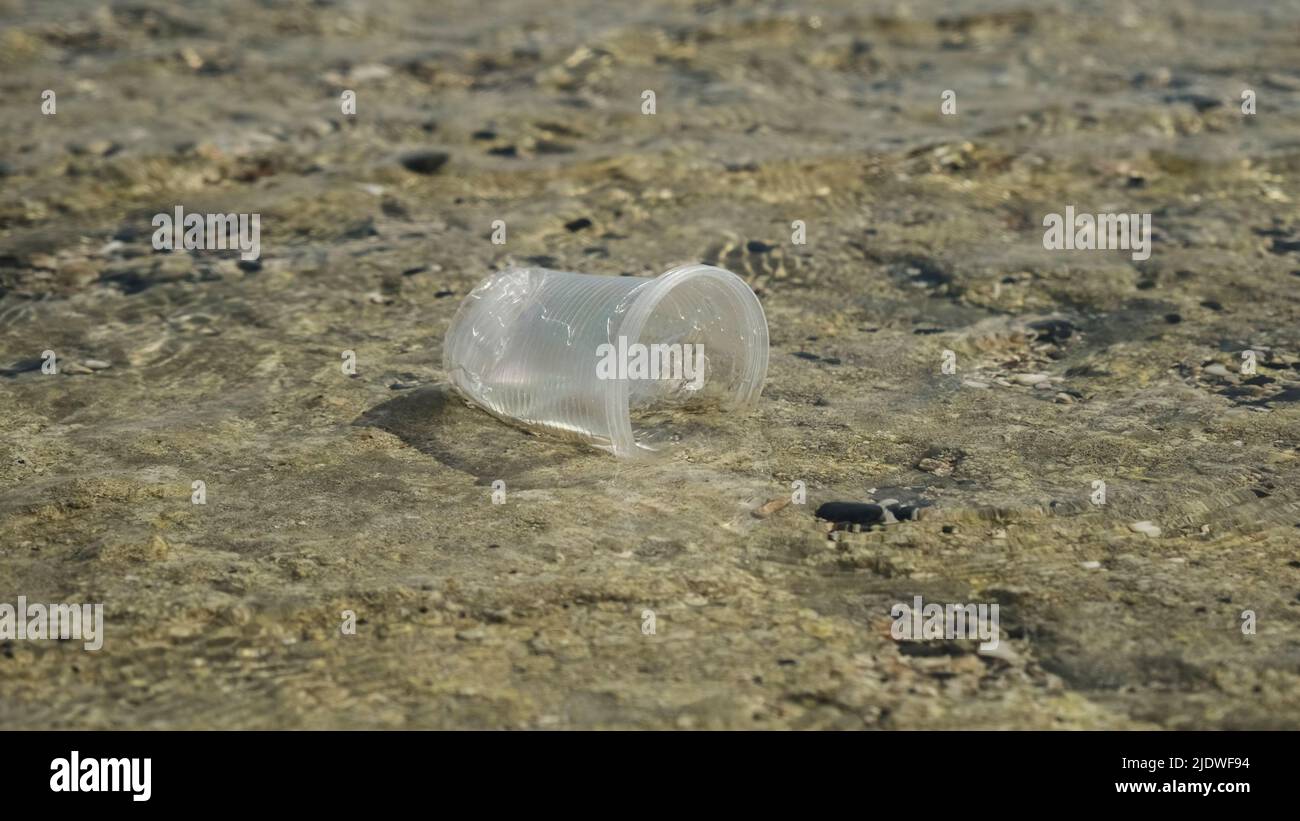 La coppa trasparente di plastica viene trasportata dal vento al mare nella zona costiera. Inquinamento plastico della zona surf. Mar Rosso, Egitto Foto Stock