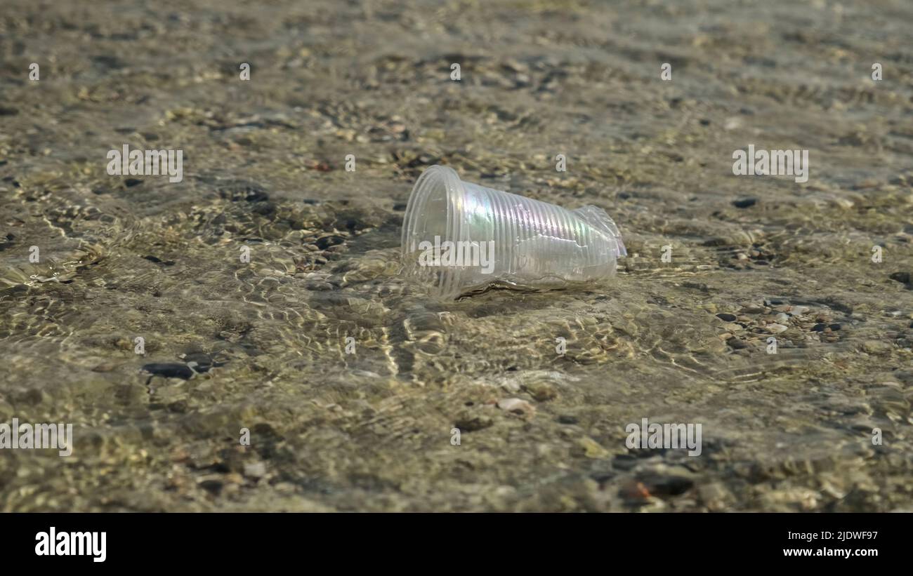 La coppa trasparente di plastica viene trasportata dal vento al mare nella zona costiera. Inquinamento plastico della zona surf. Mar Rosso, Egitto Foto Stock