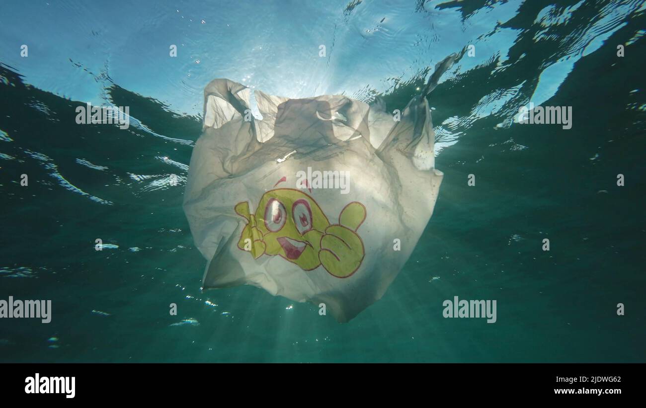 Inquinamento di plastica, sacchetto di plastica usato con il viso sorridente lentamente che si sgocciola sott'acqua ai raggi del sole all'alba. Scatto ad angolazione ridotta, retroilluminazione (Contre-jour). Plastica Foto Stock