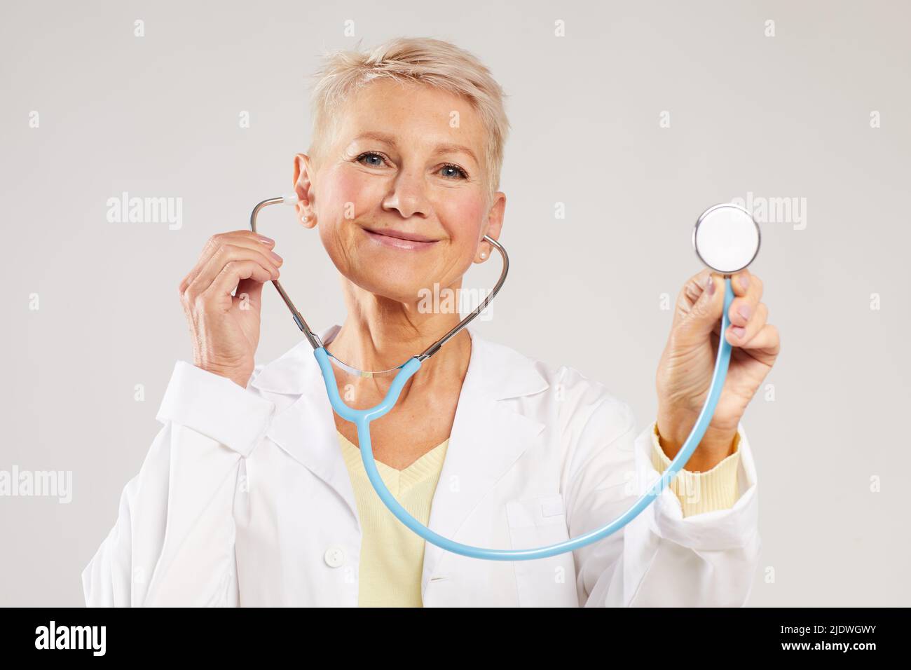 Ritratto di medico positivo maturo con capelli biondi corti usando stetoscopio per controllo medico Foto Stock