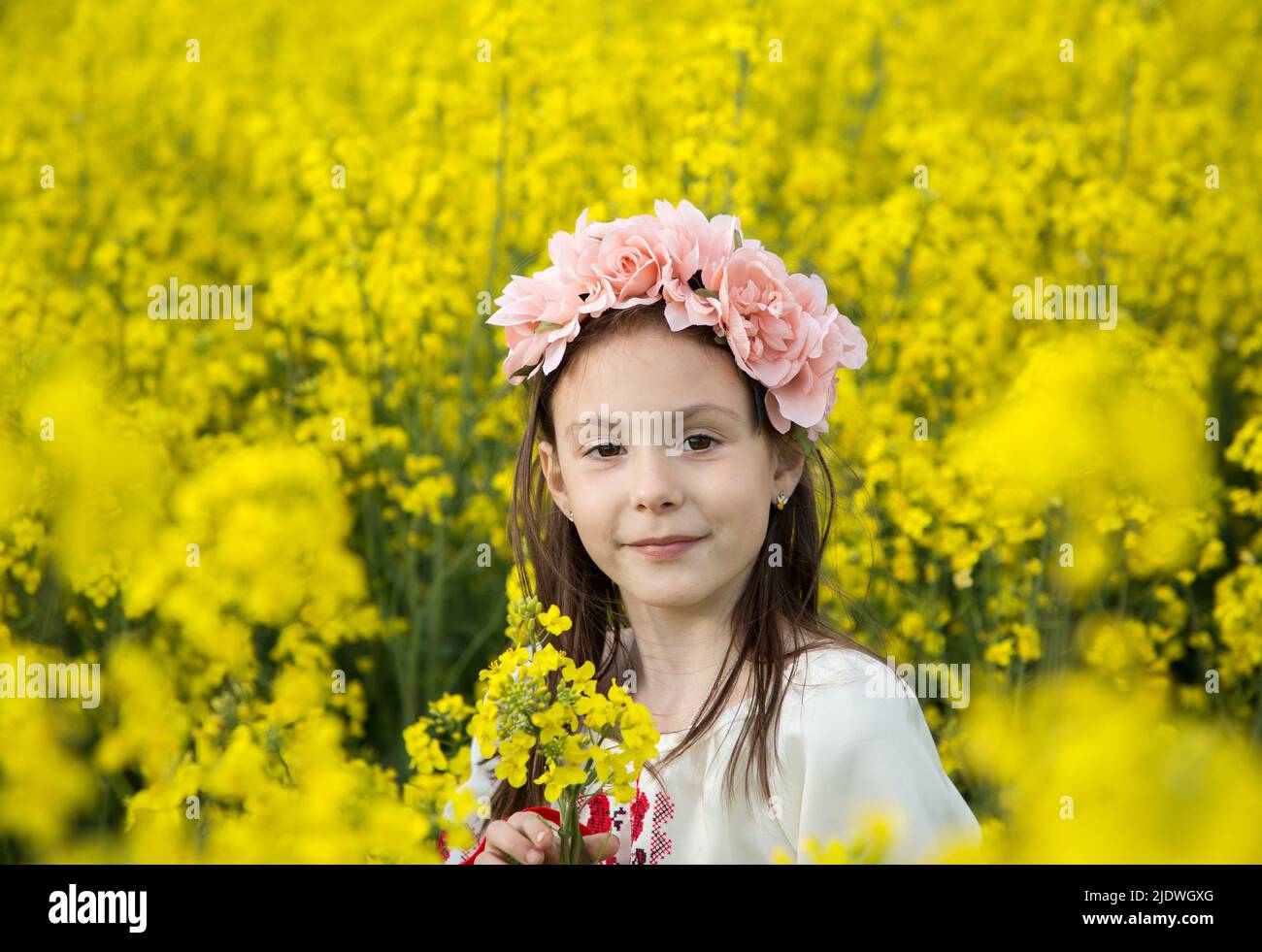 Ritratto di una ragazza ucraina carina 7 anni in una corona di fiori tra un campo di colza giallo in fiore. Bambini per la Pace. Sostenere e aiutare l'Ucraina. Foto Stock