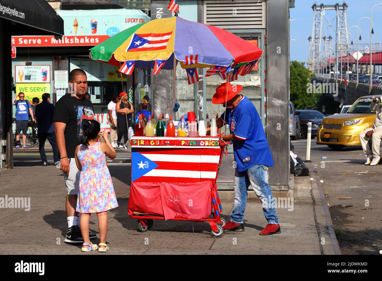 La gente che compra il piragua ha rasato il ghiaccio da un venditore di strada con un carrello colorato adornato con le bandiere di Porto Rico nel lato inferiore orientale di Manhattan, New York Foto Stock