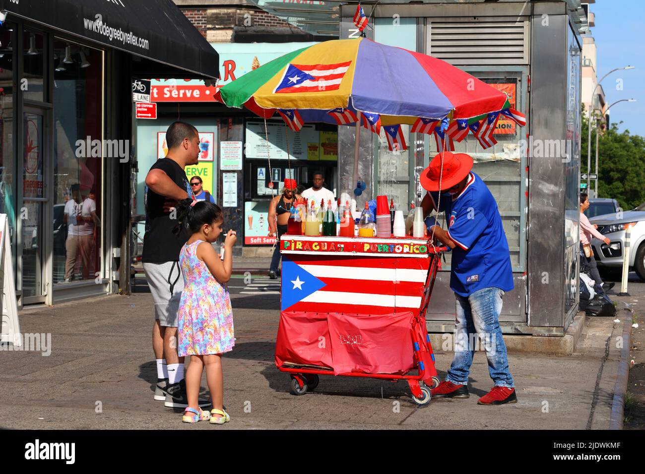 La gente che compra il piragua ha rasato il ghiaccio da un venditore di strada con un carrello colorato adornato con le bandiere di Porto Rico nel lato inferiore orientale di Manhattan, New York Foto Stock