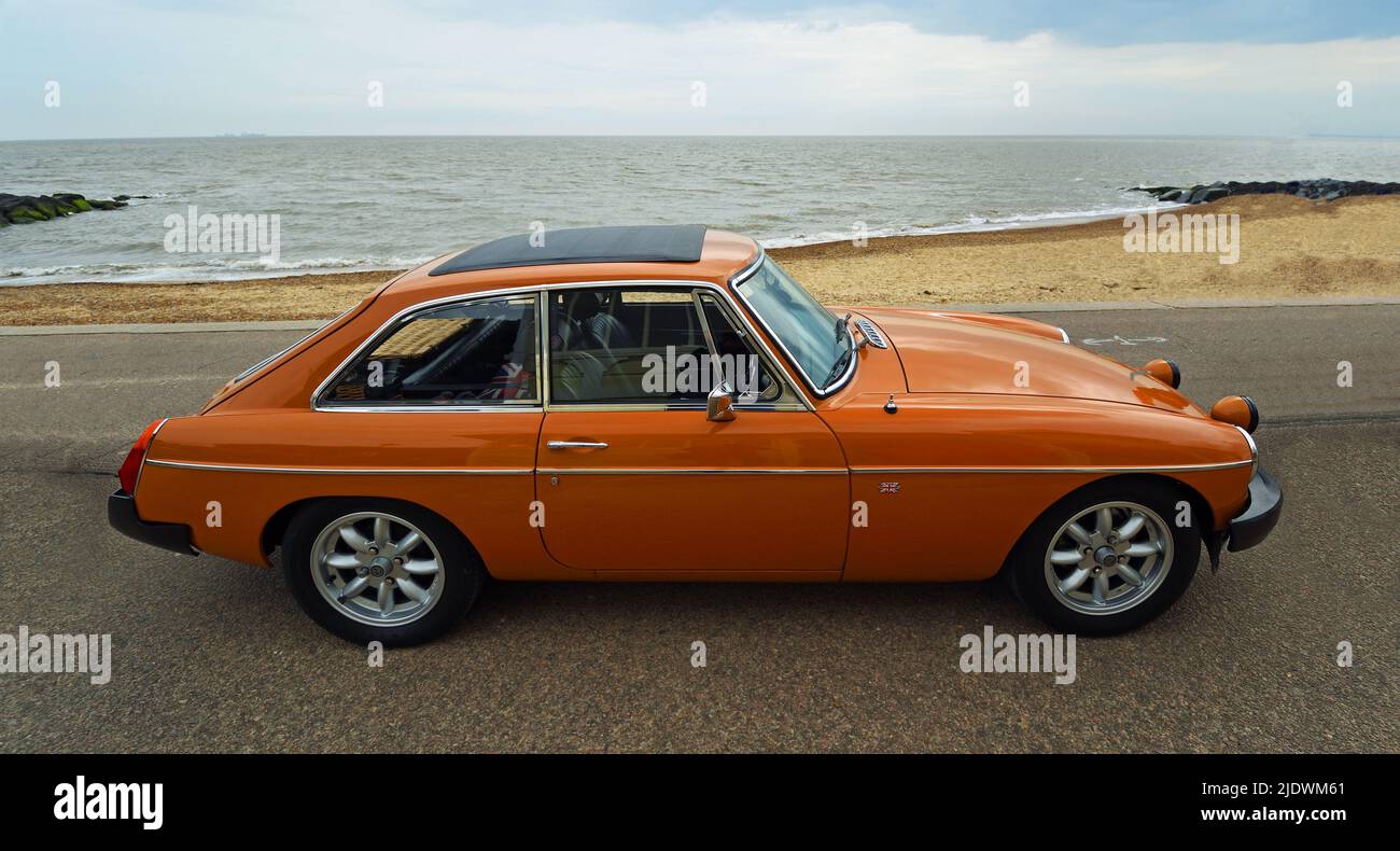 Classic Orange MGB GT parcheggiato sulla spiaggia lungomare e l'oceano sullo sfondo. Foto Stock
