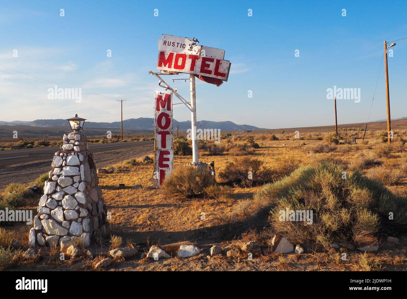 Olancha, USA - 06.06.2016: Vecchio segno di metallo bianco e rosso accanto alla strada nel deserto dicendo Motel rustico. Cartello d'alloggio sotto il cielo blu su un caldo Foto Stock