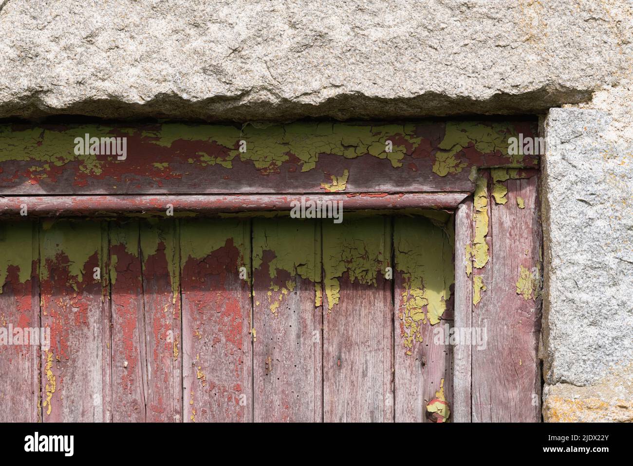 L'angolo superiore di una vecchia porta di legno giallo-verde, incorniciata da blocchi di granito, con vernice spaccata che mostra un colore di Crimson e Woodworm intemperie Foto Stock