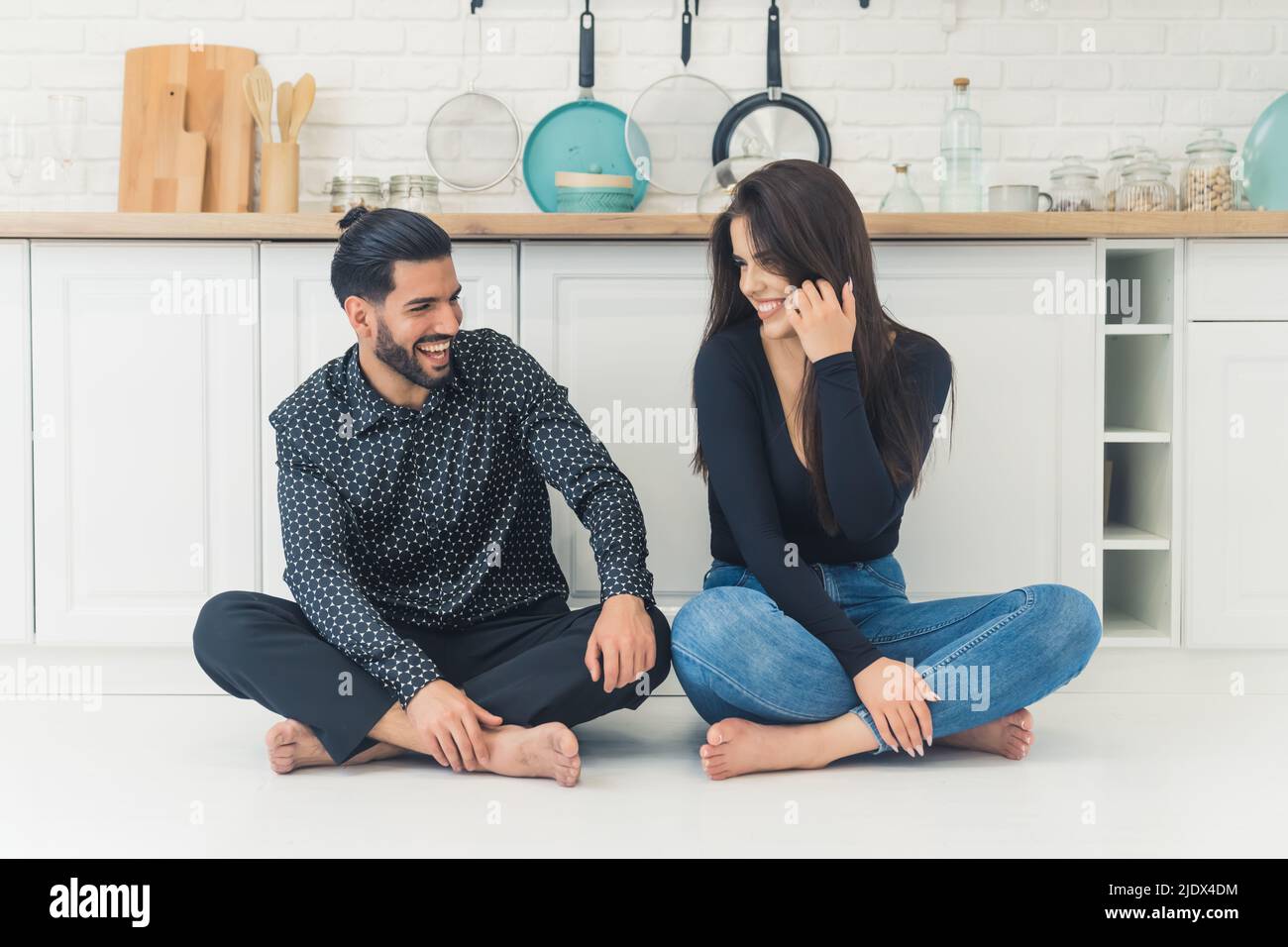 Allegro millenario interrazziale coppia sposata seduta a piedi nudi sul pavimento con le loro gambe incrociate, sorridenti e parlare insieme. Foto di alta qualità Foto Stock