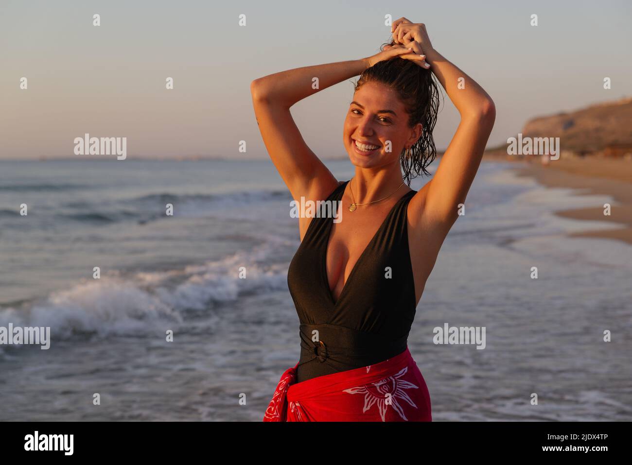 Felice, giovane donna in costume nero si diverte sulla spiaggia all'alba Foto Stock