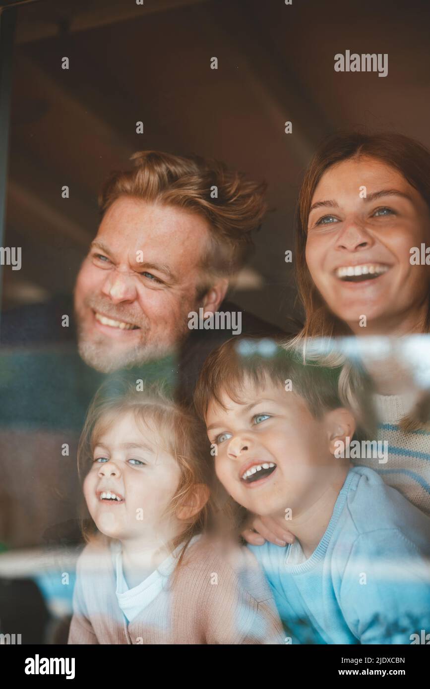 Genitori e bambini felici che premono i volti sul vetro della finestra Foto Stock