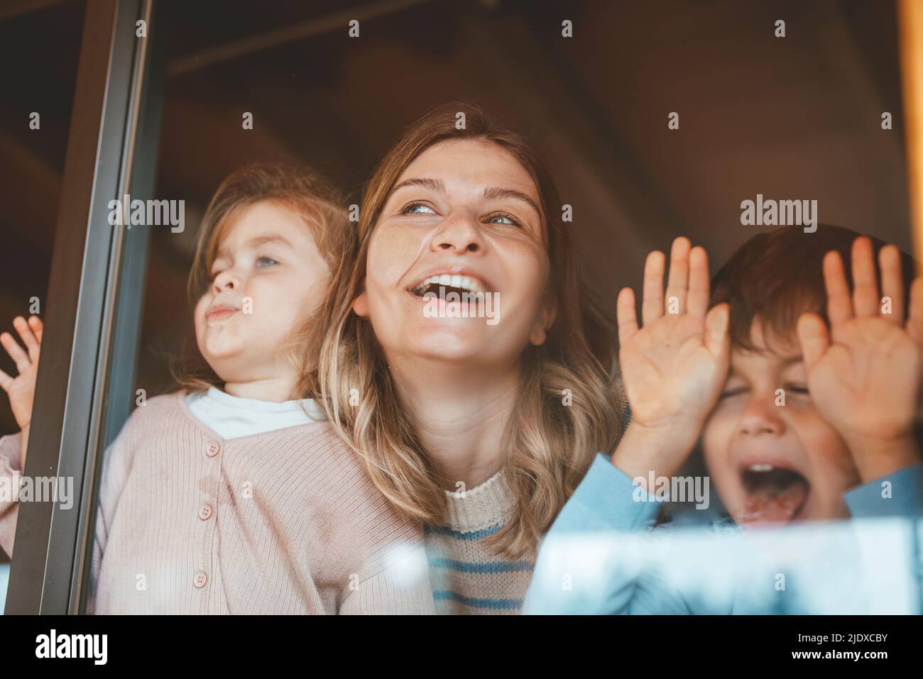 Donna giocosa con figlia e figlio che premono i volti sulla finestra di vetro Foto Stock