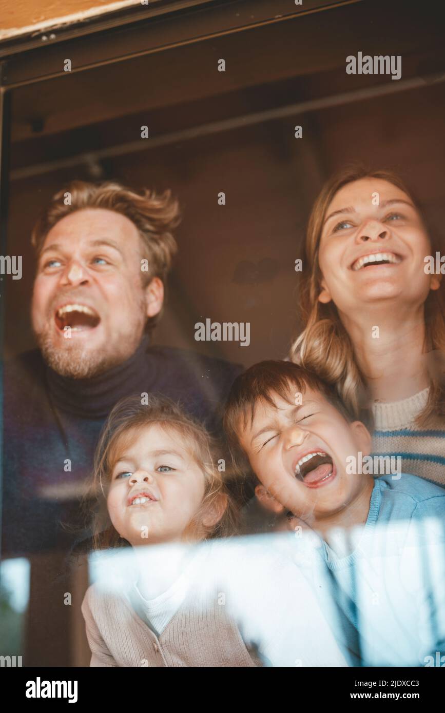 Genitori e bambini giocosi che premono i volti sul vetro della finestra Foto Stock