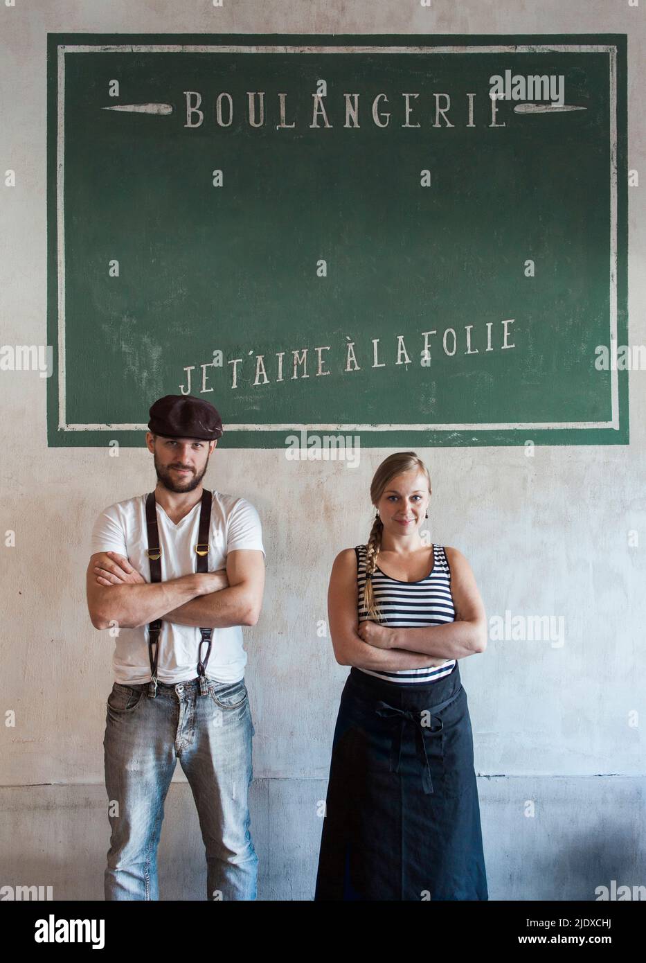 Proprietari di panetteria fiduciosi in piedi con le braccia incrociate di fronte al muro con testo francese Foto Stock