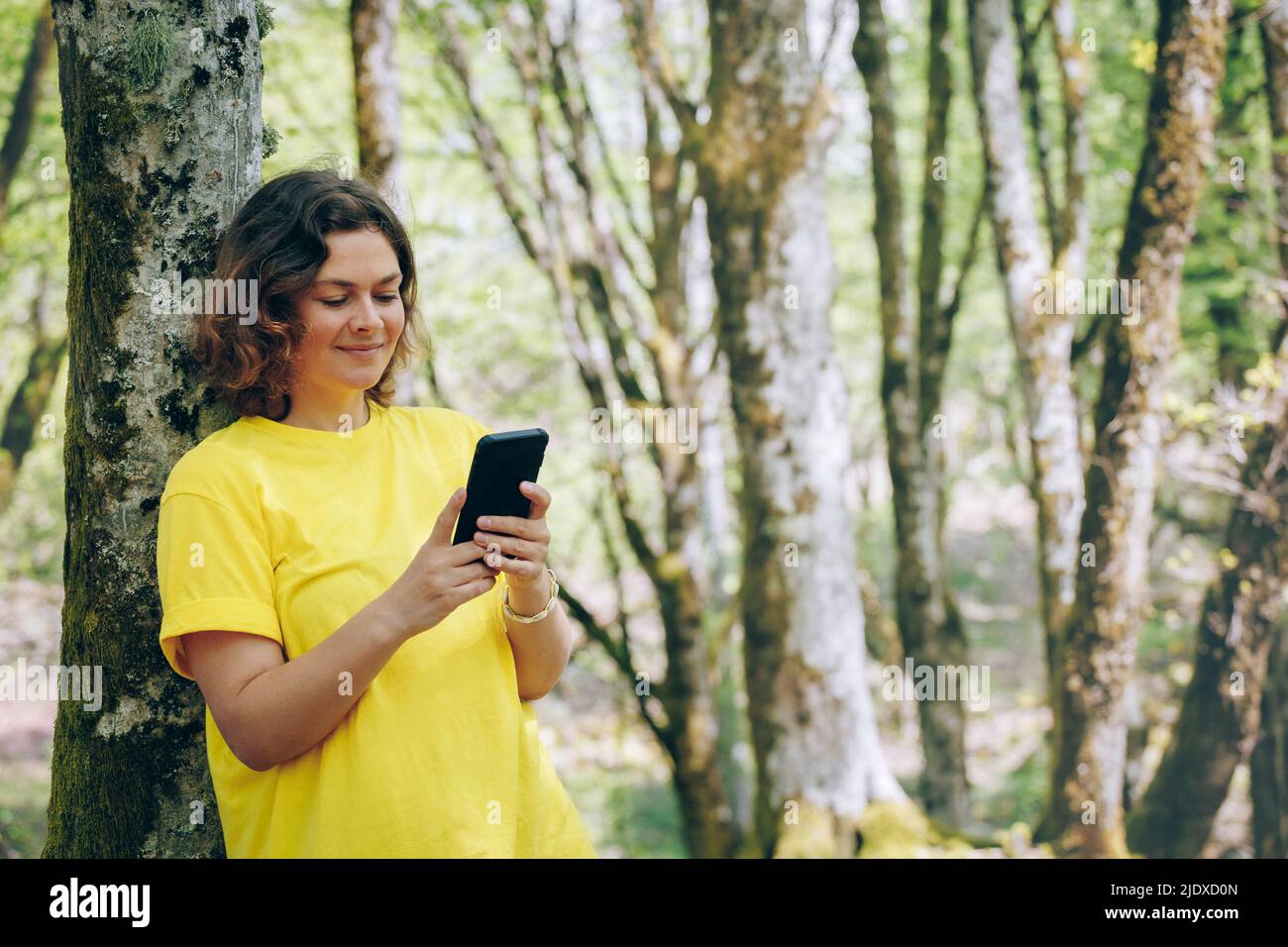 Donna sorridente messaggi di testo sul telefono cellulare nella foresta Foto Stock