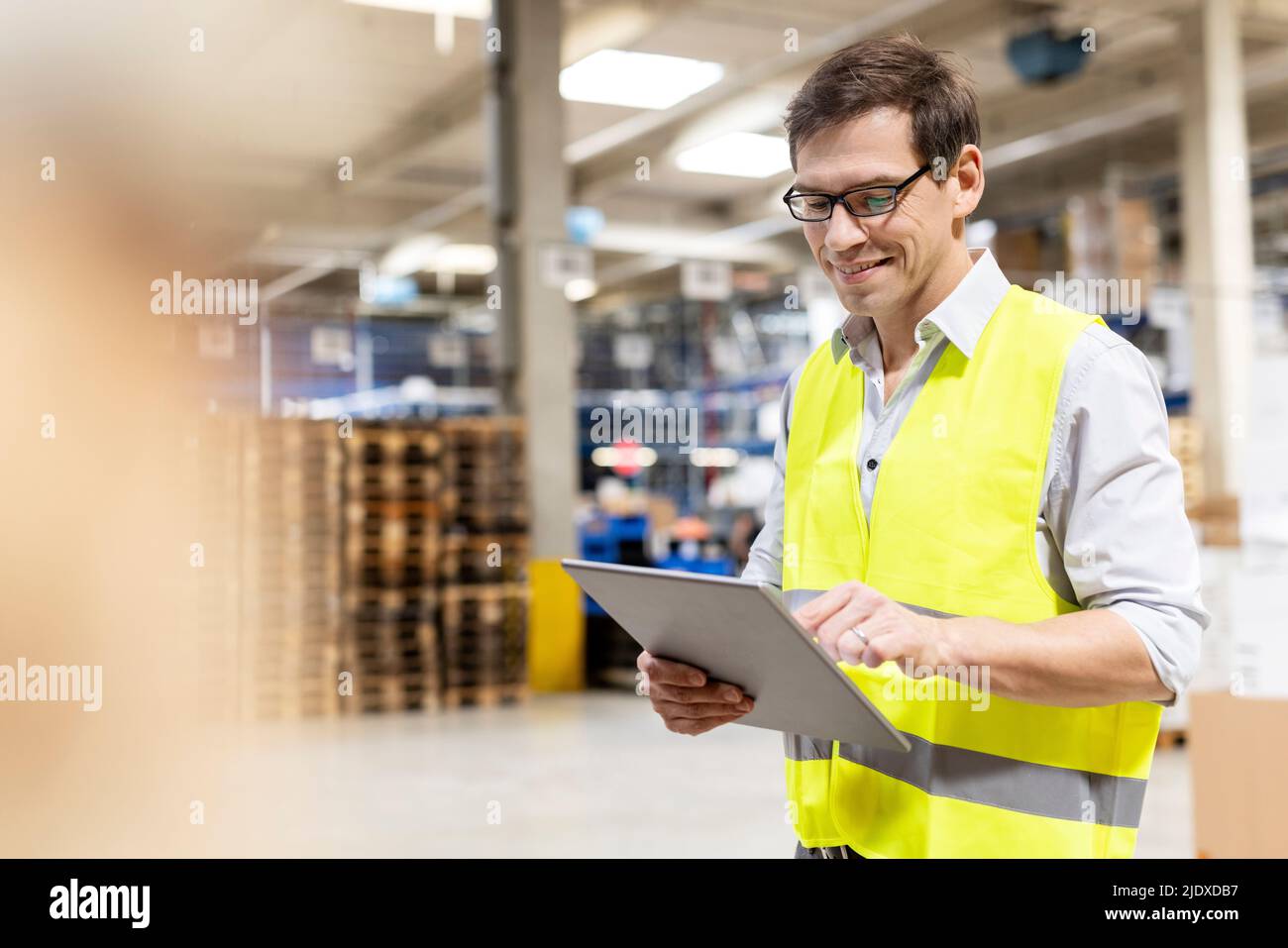Sorridente lavoratore che indossa occhiali utilizzando un tablet PC in magazzino Foto Stock
