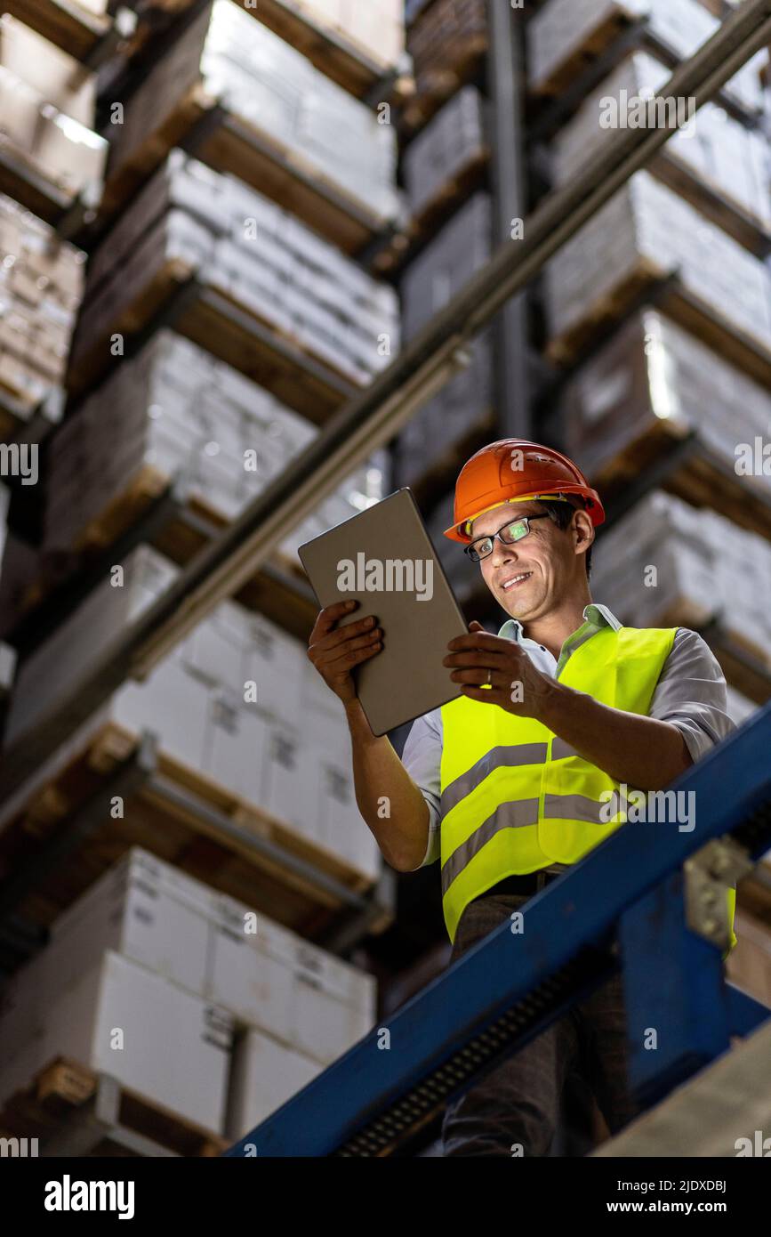 Sorridente lavoratore che indossa occhiali con tablet PC in magazzino Foto Stock