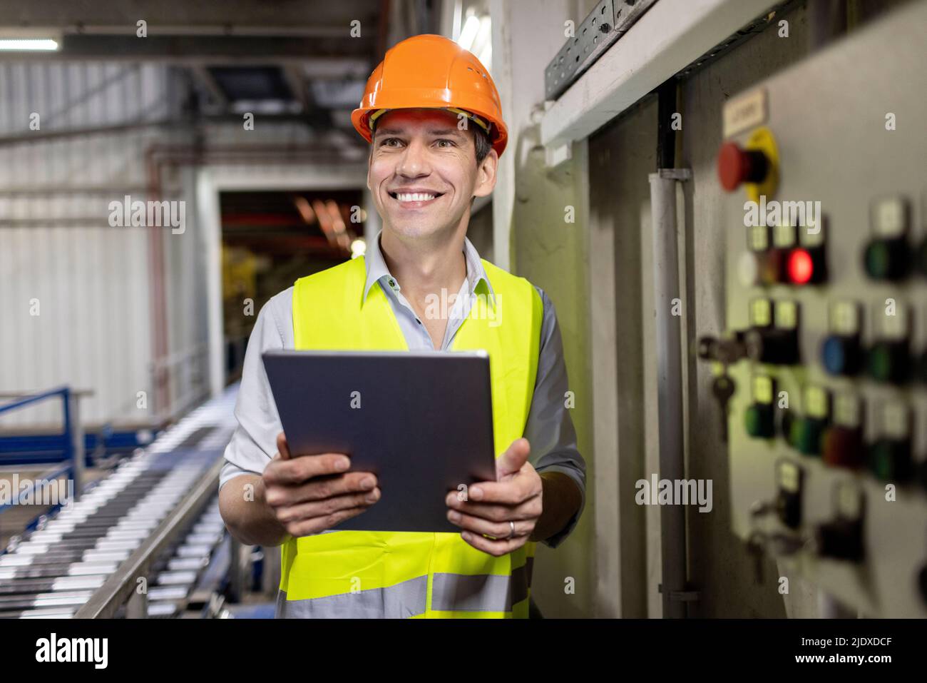 Un lavoratore felice che indossa un elmetto in piedi con un tablet PC in magazzino Foto Stock