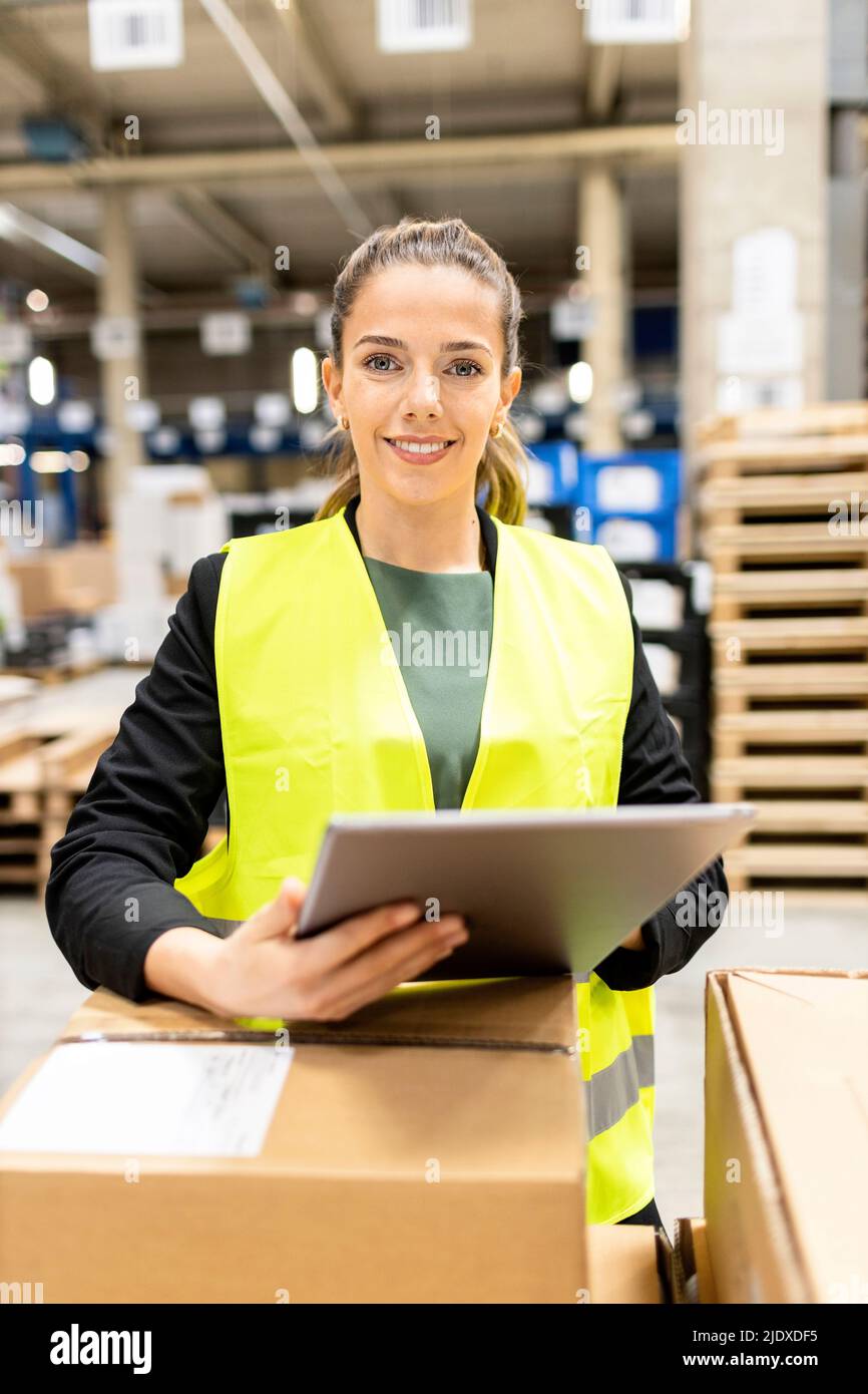 Sorridente lavoratore giovane con tablet PC in piedi da scatola di cartone in magazzino Foto Stock