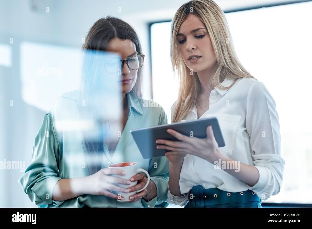 Donna d'affari che condivide idee con i colleghi rispetto ai tablet PC in ufficio Foto Stock