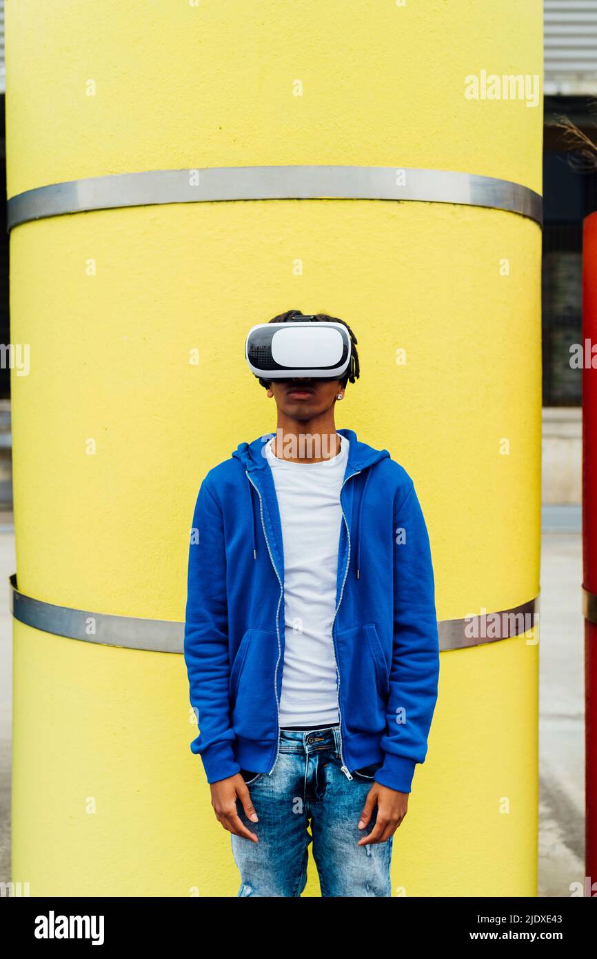 Uomo che indossa simulatore di realtà virtuale in piedi di fronte al tubo giallo in calcestruzzo Foto Stock