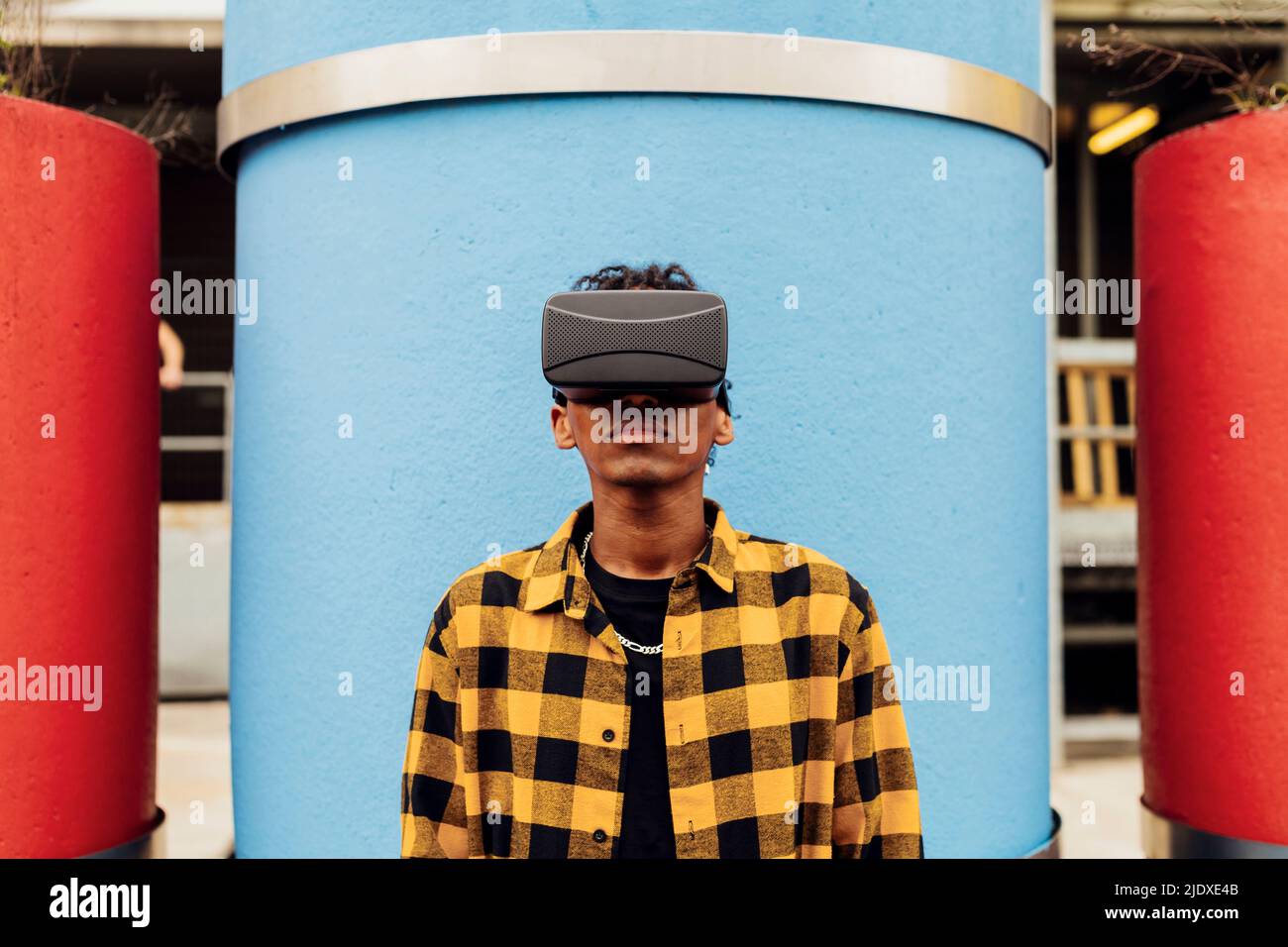 Uomo che indossa simulatore di realtà virtuale in piedi di fronte al tubo di cemento blu Foto Stock