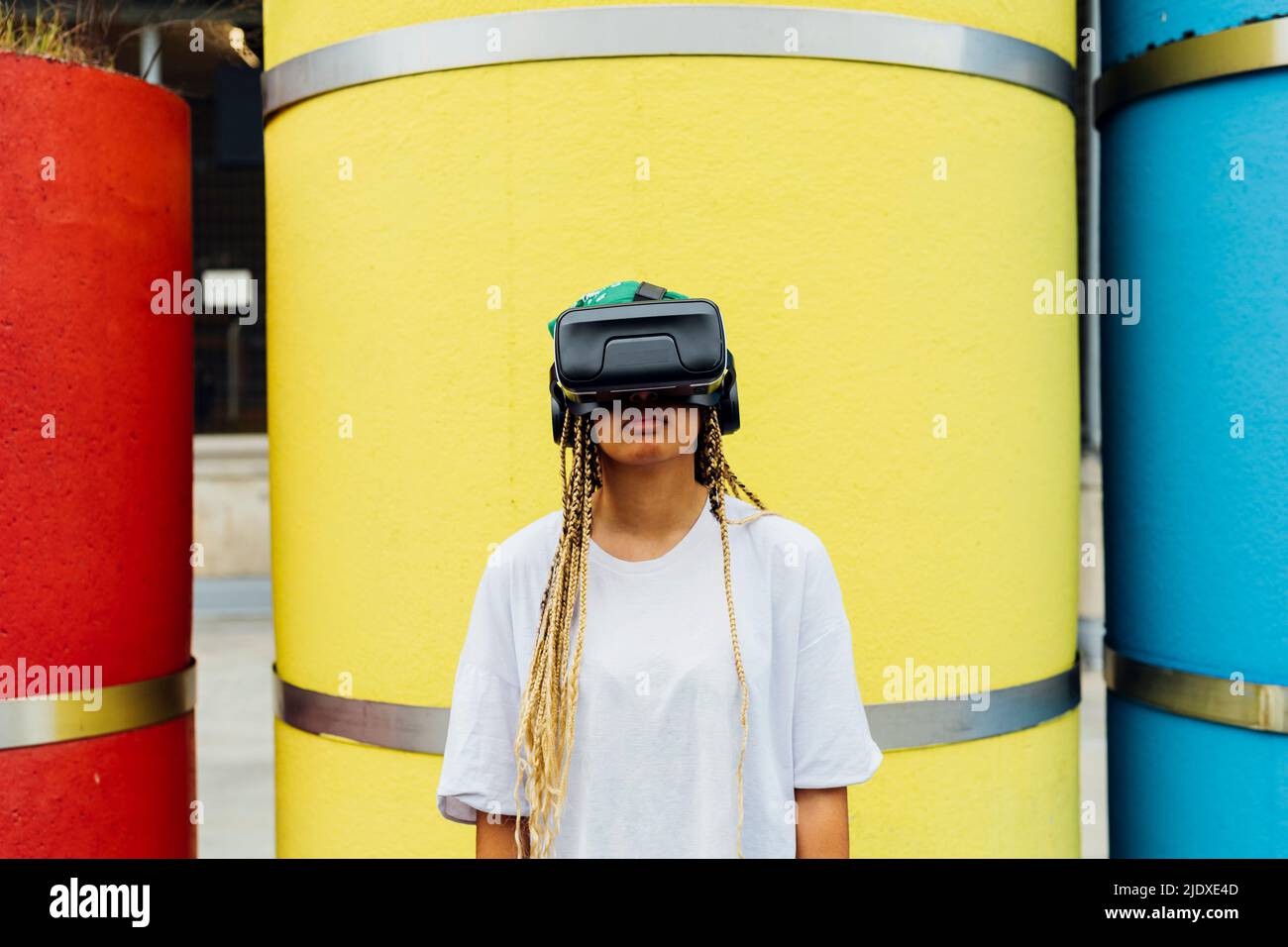 Giovane donna che indossa simulatore di realtà virtuale in piedi di fronte al tubo giallo in calcestruzzo Foto Stock