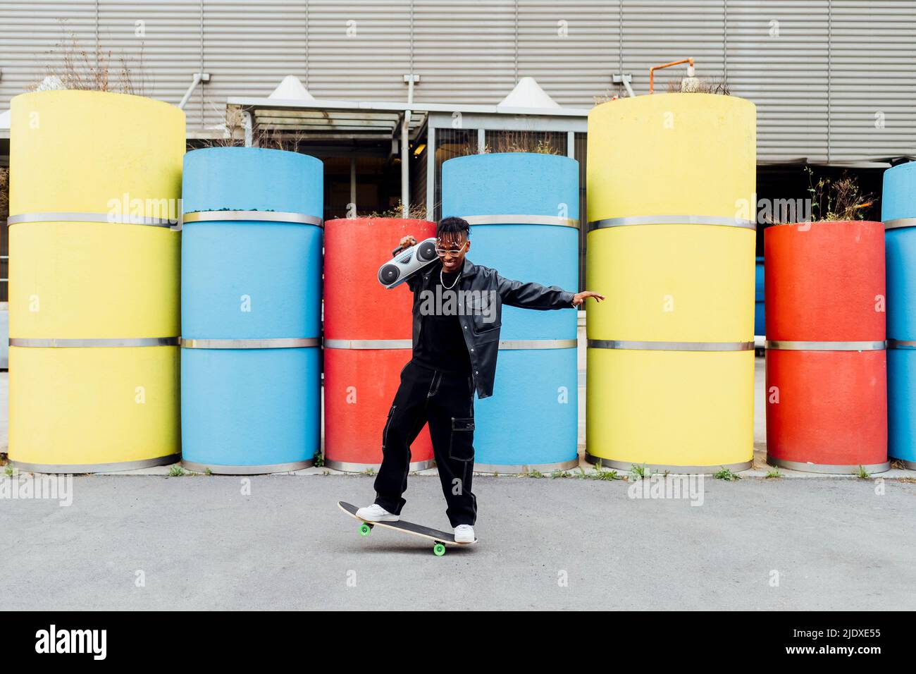 Buon giovane uomo con boom box in equilibrio sullo skateboard di fronte a tubi in calcestruzzo Foto Stock