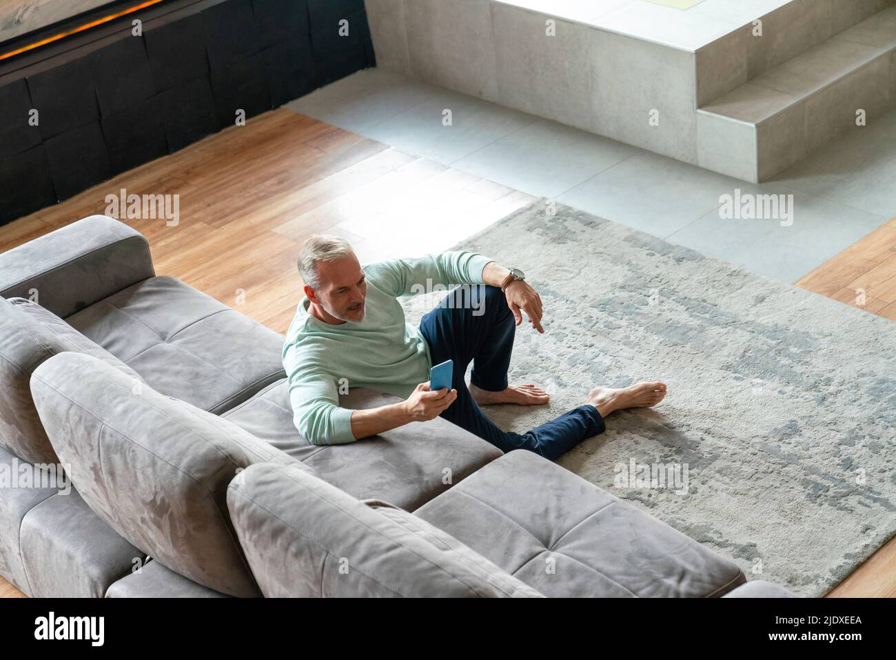 Uomo che usa uno smartphone appoggiato sul divano nel soggiorno di casa Foto Stock