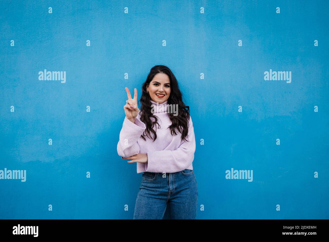 Sorridente giovane bella donna che mostra il numero 2 di fronte al muro blu Foto Stock