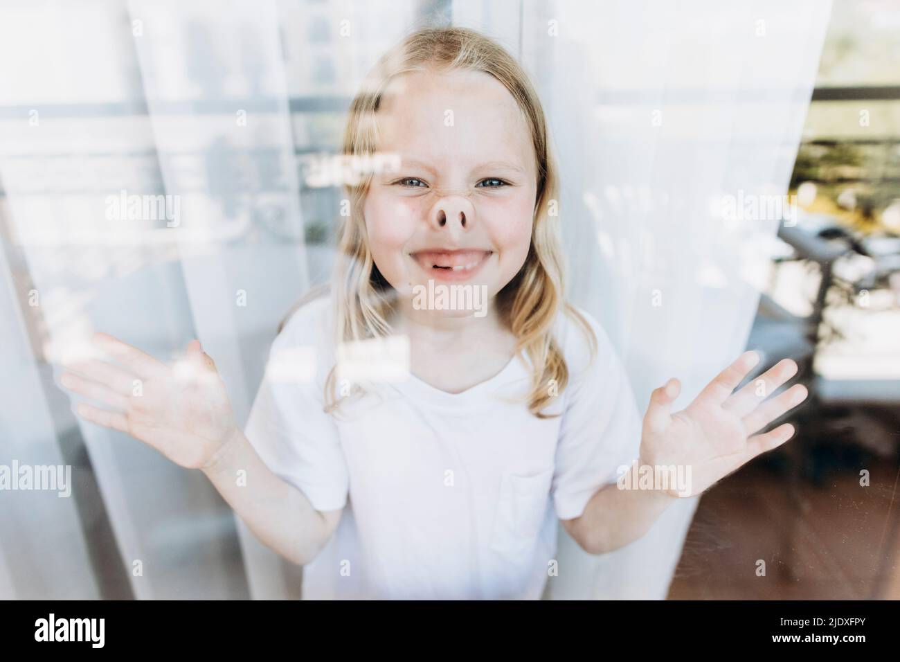 Ragazza giocosa che fa i volti in piedi dalla finestra a casa Foto Stock