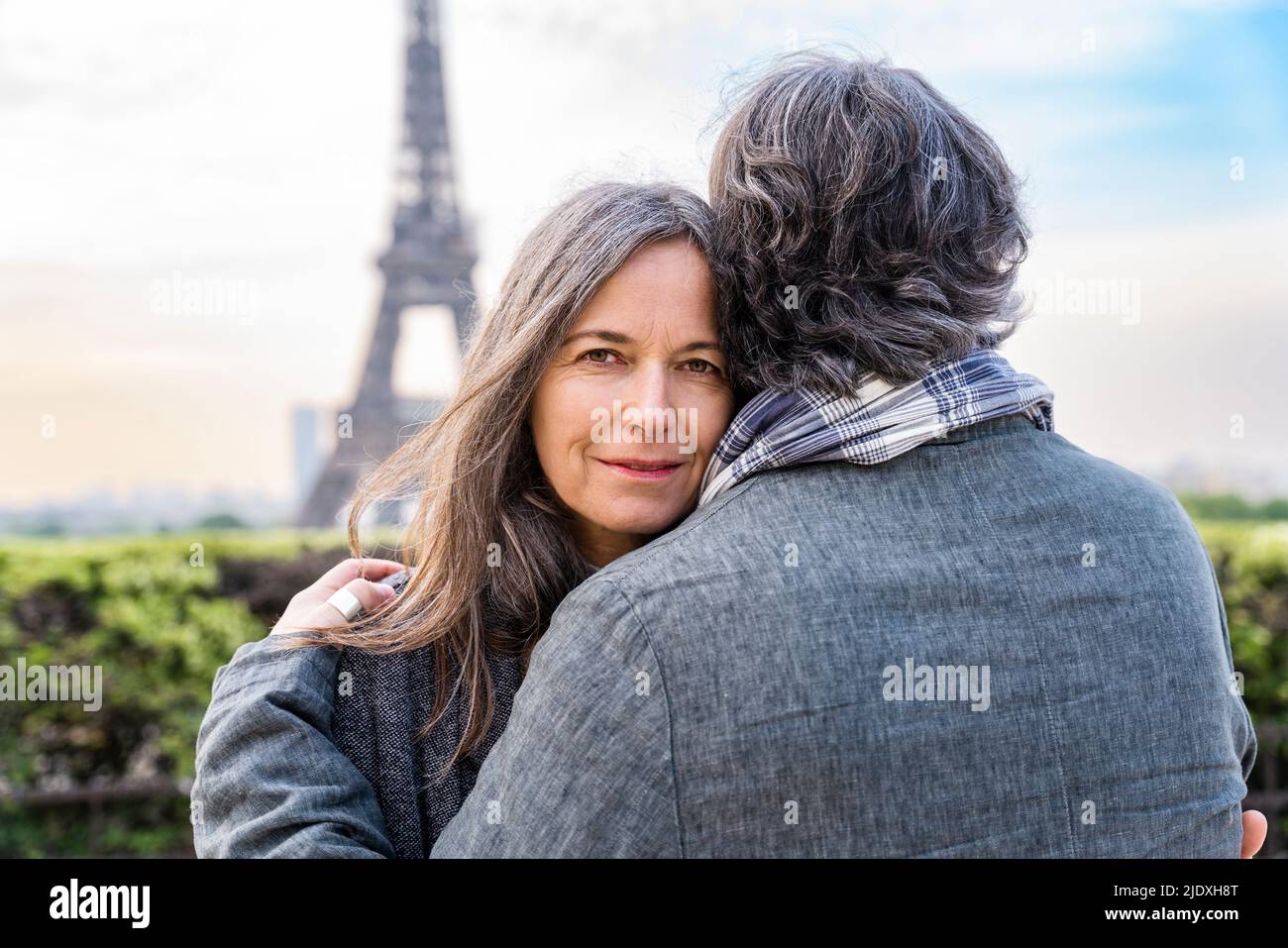 Donna matura sorridente che abbraccia l'uomo di fronte alla Torre Eiffel, Parigi, Francia Foto Stock