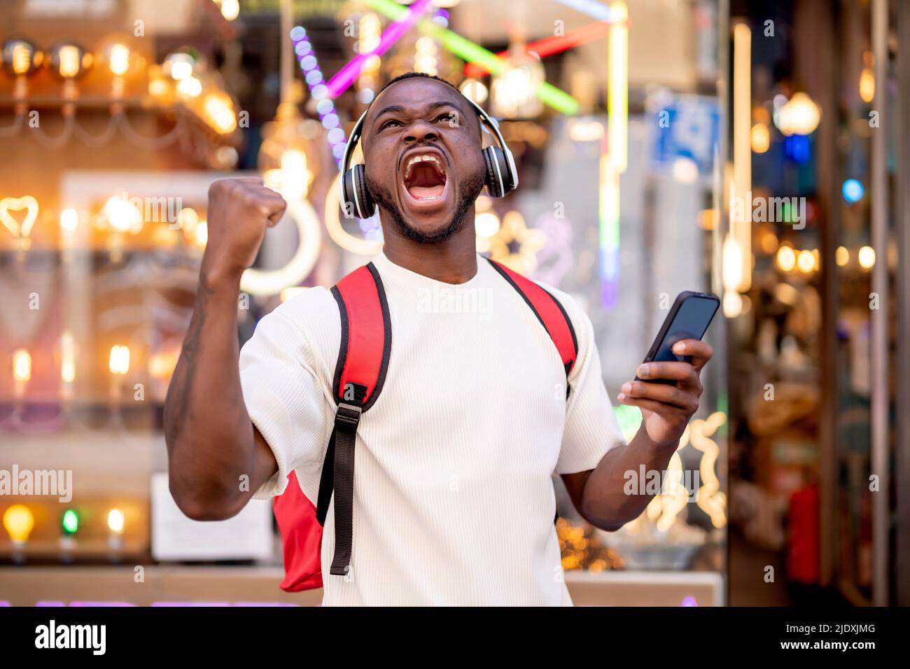 Uomo emozionato con cuffie e smart phone che stringono il pugno davanti alle luci al neon Foto Stock