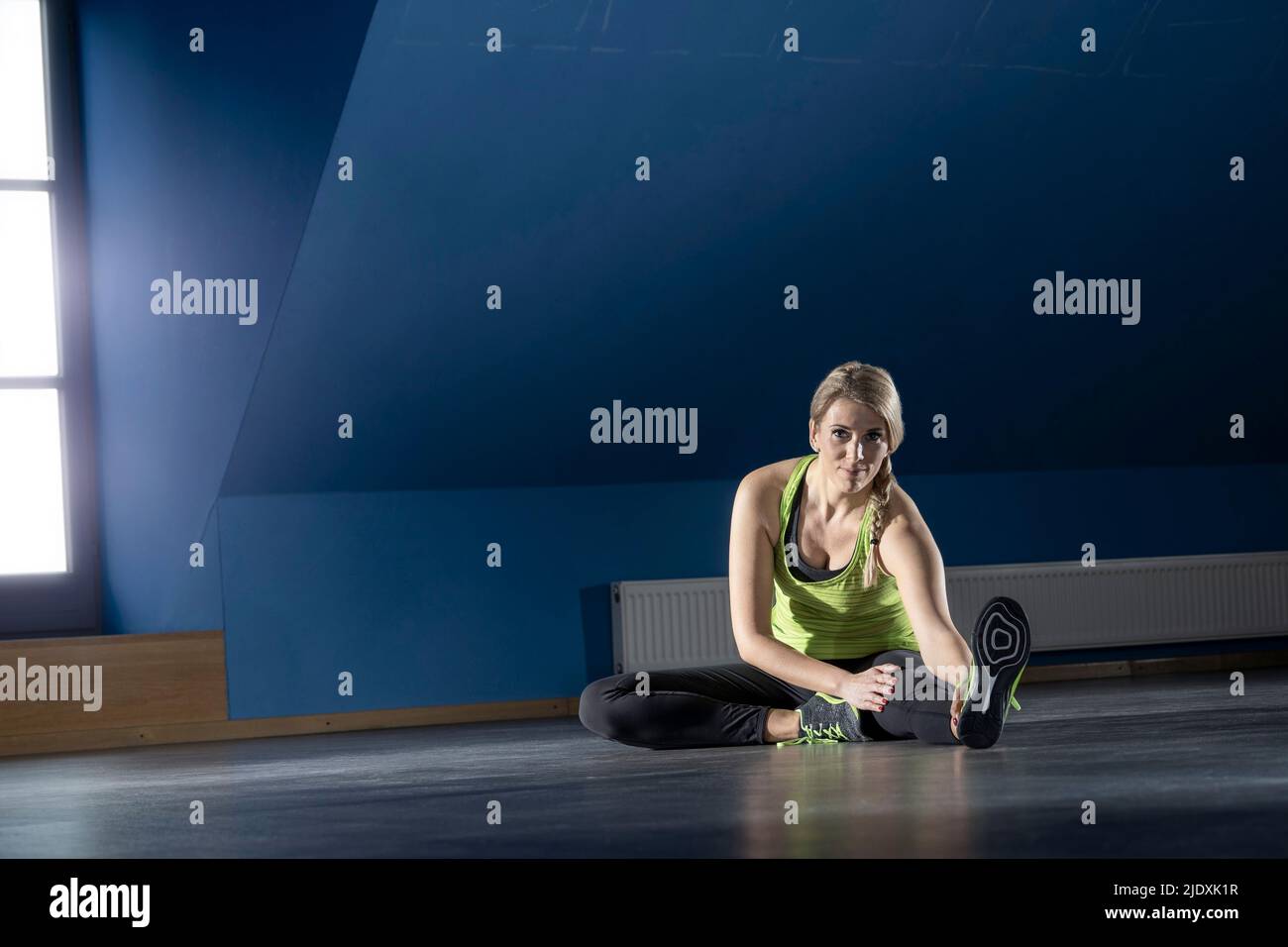 Donna che fa esercizio stretching seduta sul pavimento nella sala fitness Foto Stock