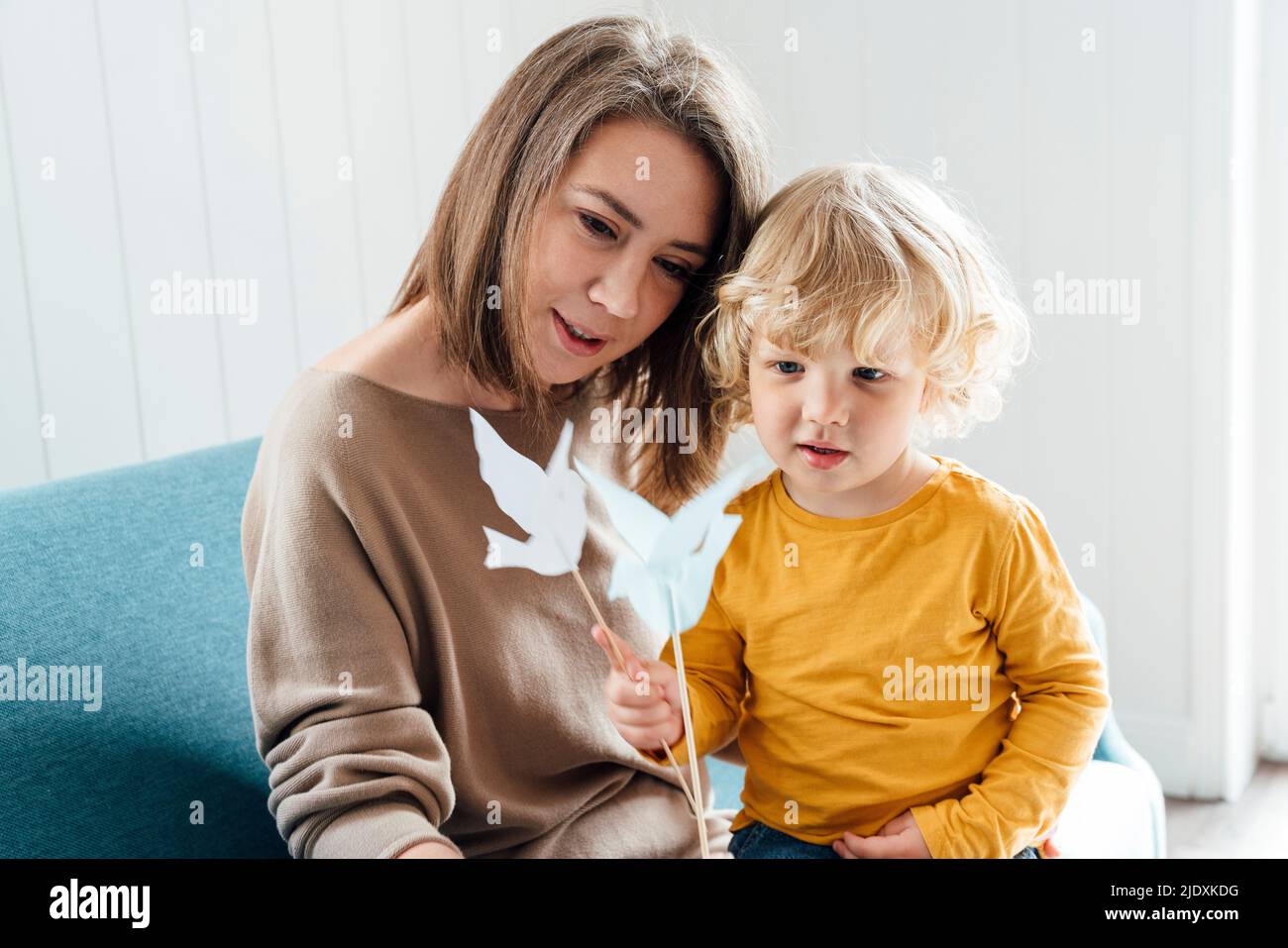 Madre con figlio che tiene uccelli origami seduti sul divano a casa Foto Stock
