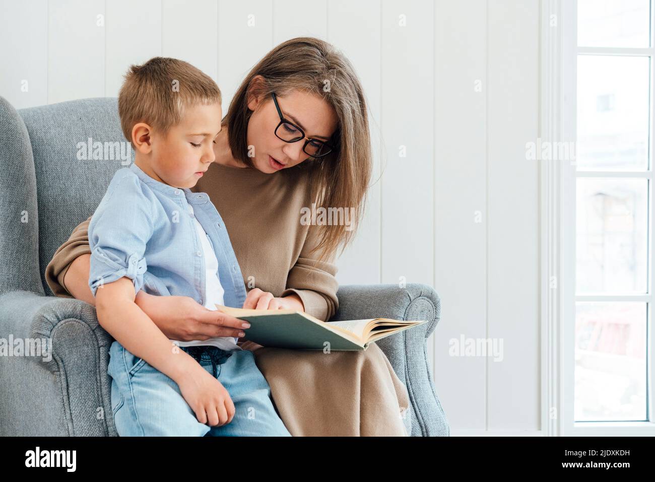 Madre con figlio leggere libro seduta su poltrona a casa Foto Stock