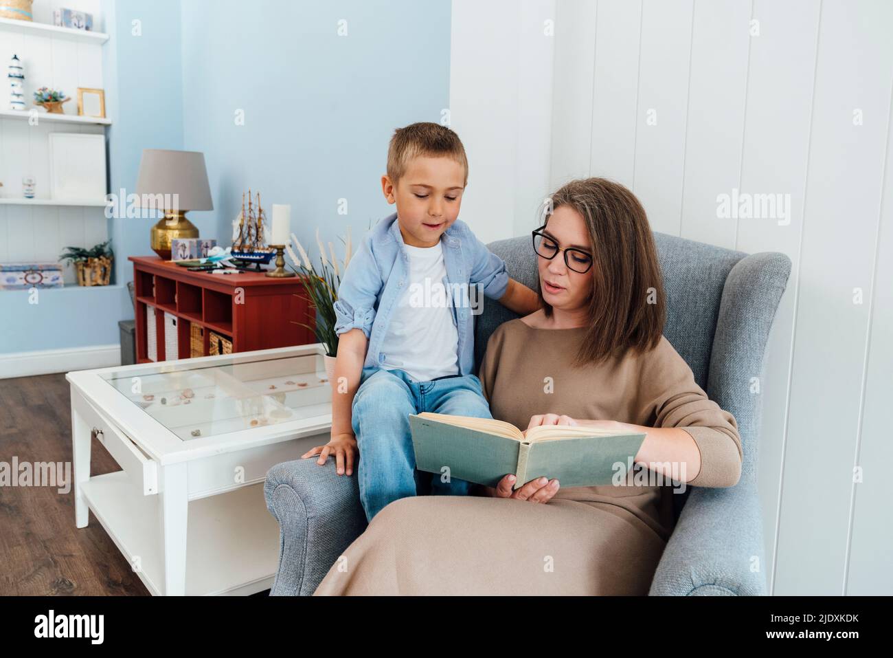 Madre leggere libro a figlio seduto su poltrona a casa Foto Stock