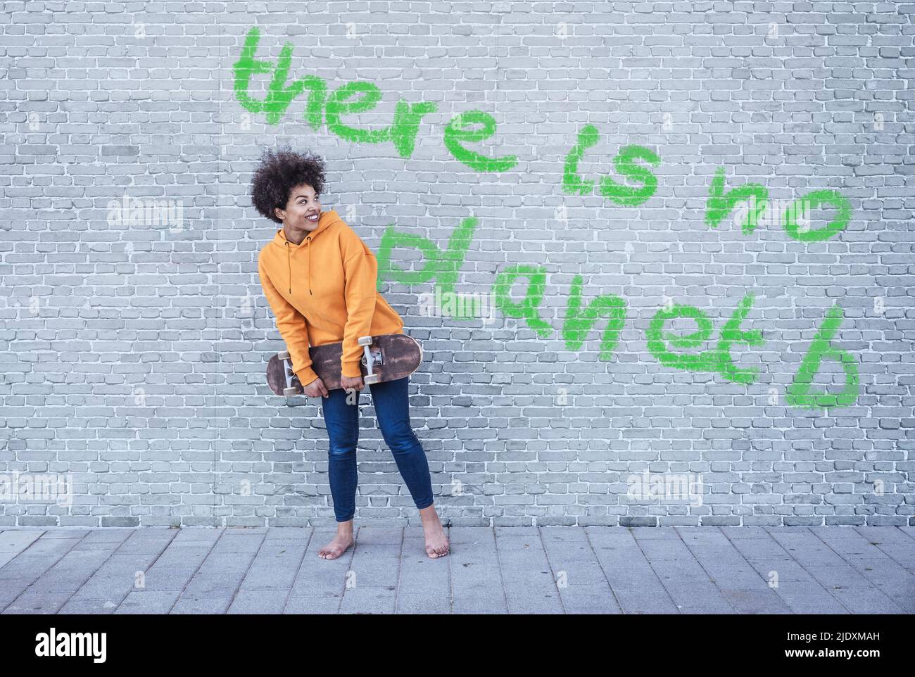 Donna che tiene lo skateboard di fronte al muro con testo non c'è Planet B. Foto Stock